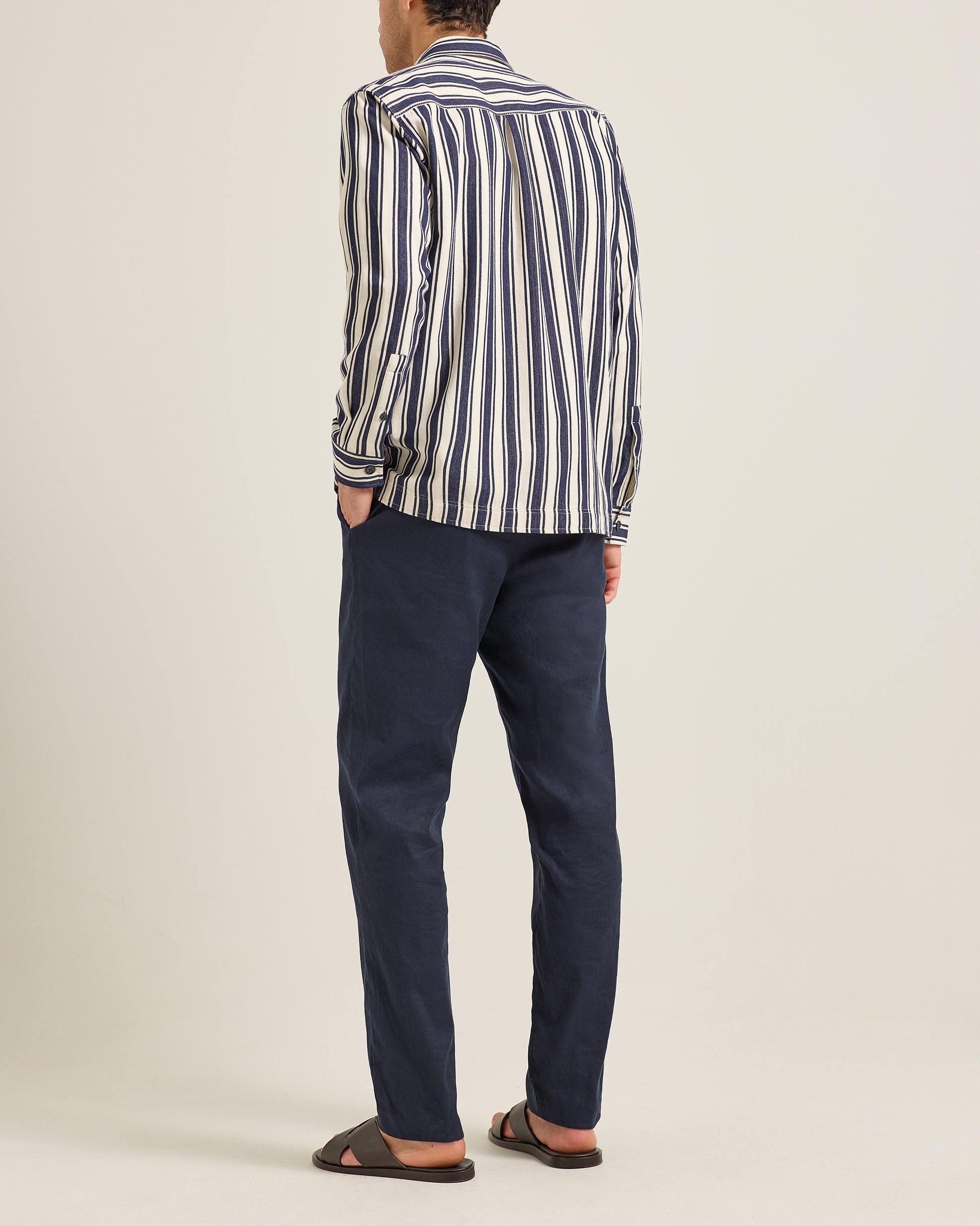 Person wearing a striped shirt and dark pants on a plain background