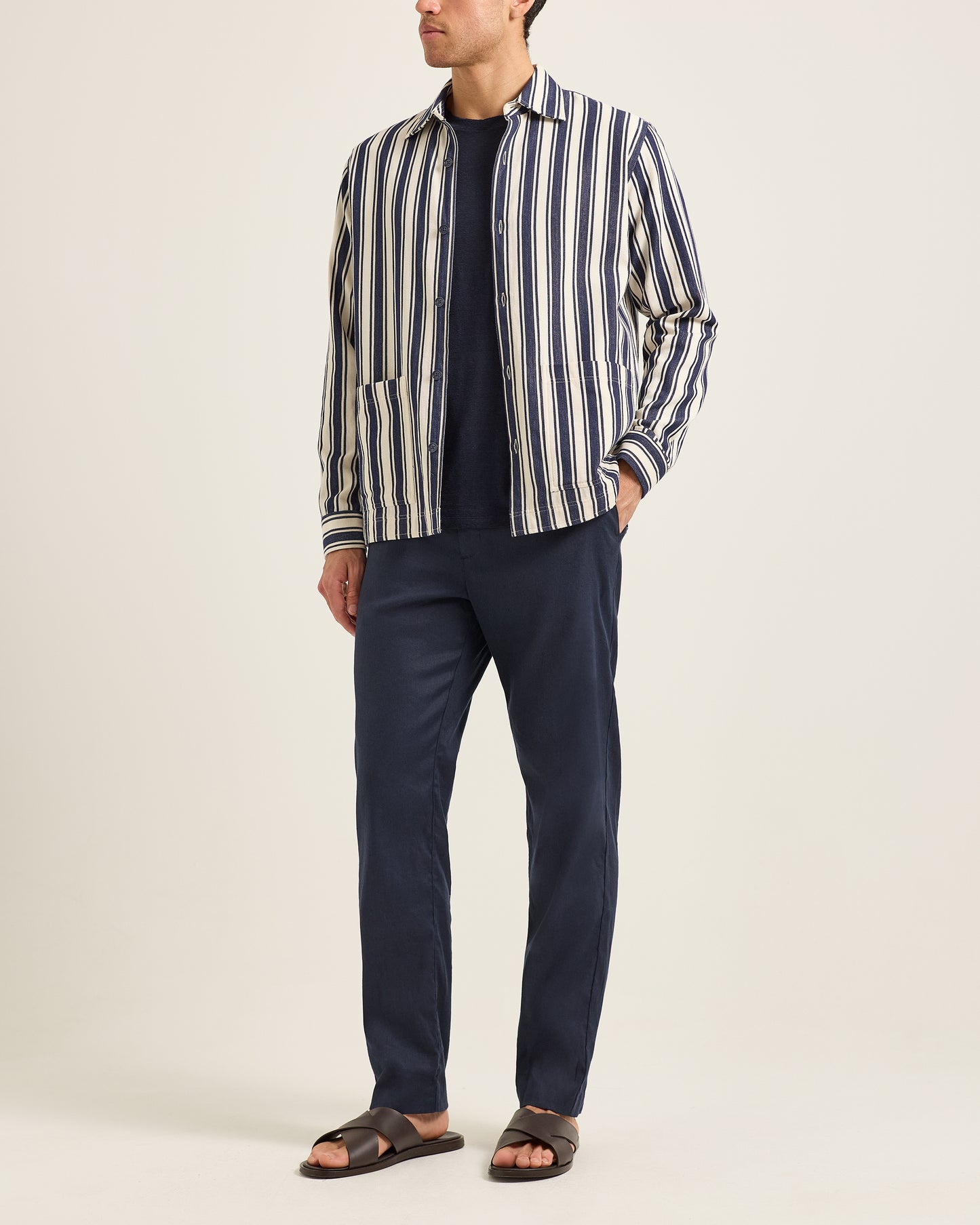 Man wearing a striped shirt and navy pants on a plain background