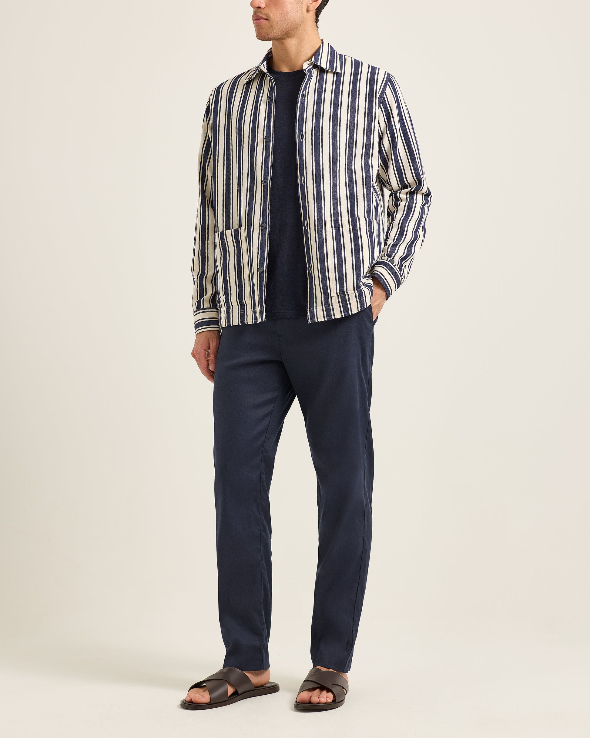 Man wearing a striped shirt and navy pants on a plain background
