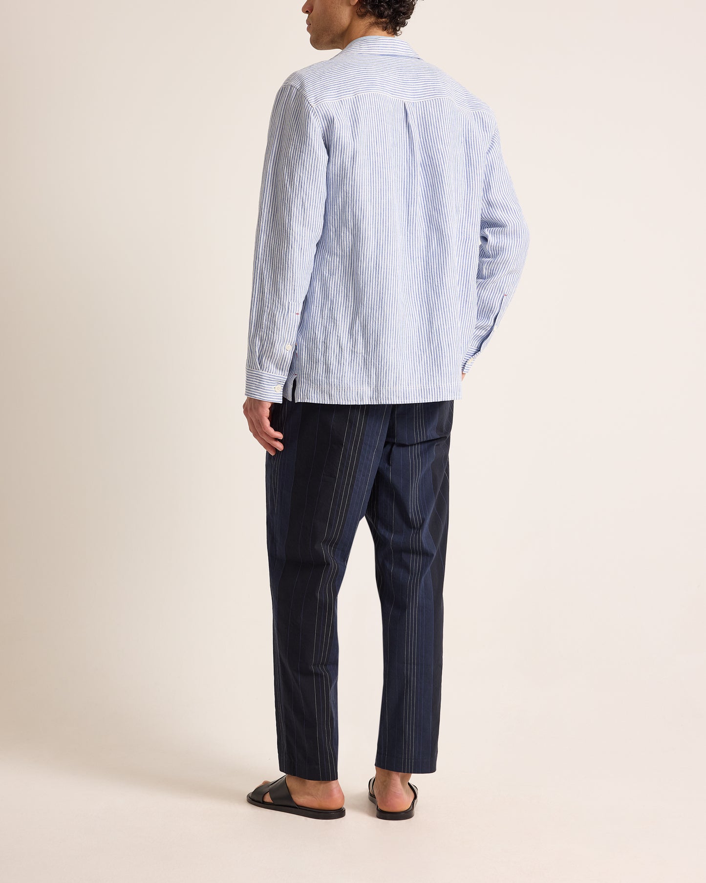 Person wearing a light blue striped shirt and dark pinstripe pants on a beige background