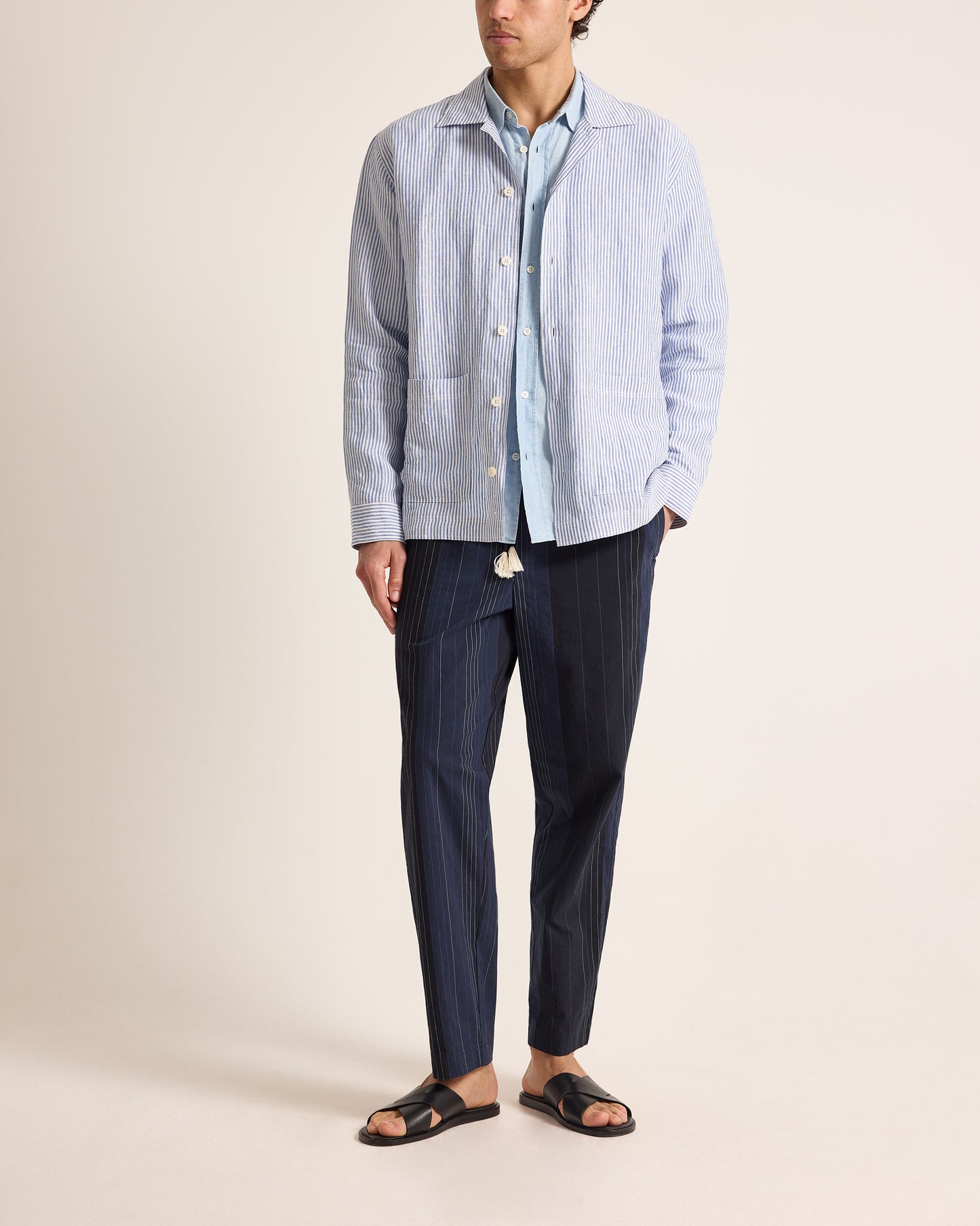 Person wearing a light blue striped shirt and dark blue pants on a beige background