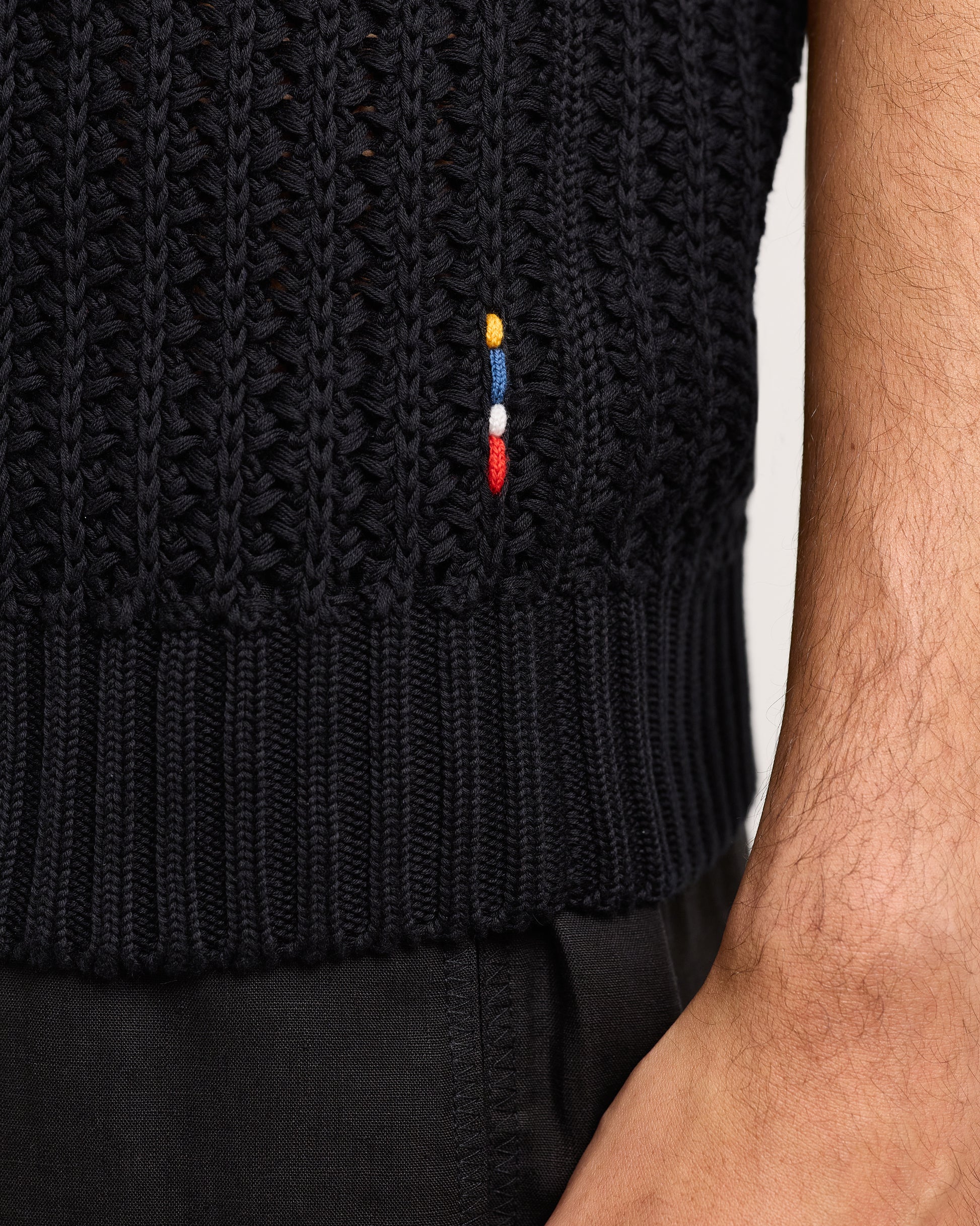 Black knitted vest with an embroidered design on a neutral background