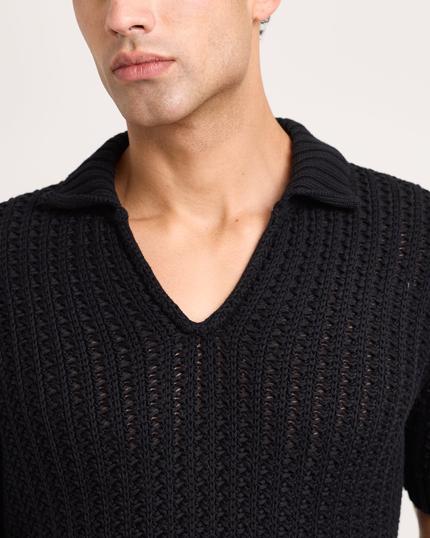 Black knitted polo shirt worn by a person on a plain background