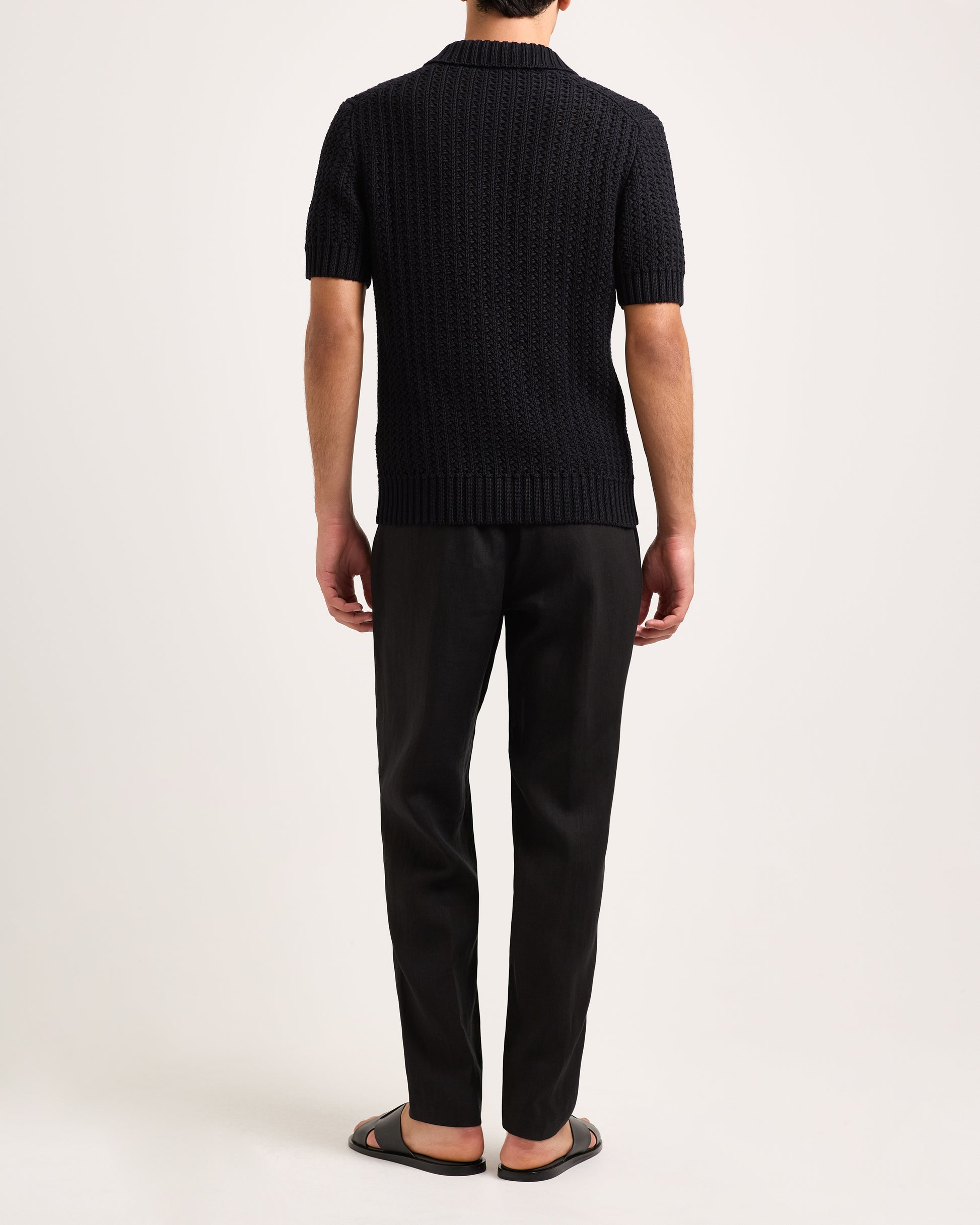Person wearing a black knitted polo and black pants on a white background