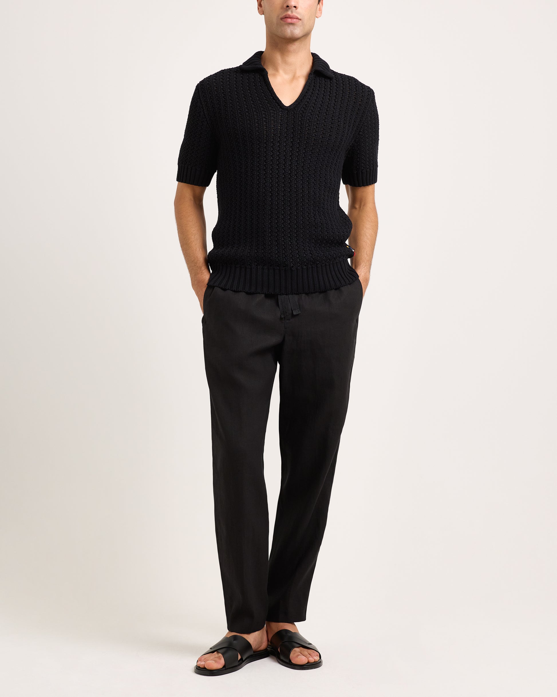 Person wearing a black knitted polo and black pants on a white background