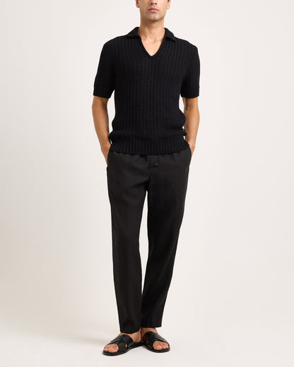 Person wearing a black knitted polo and black pants on a white background