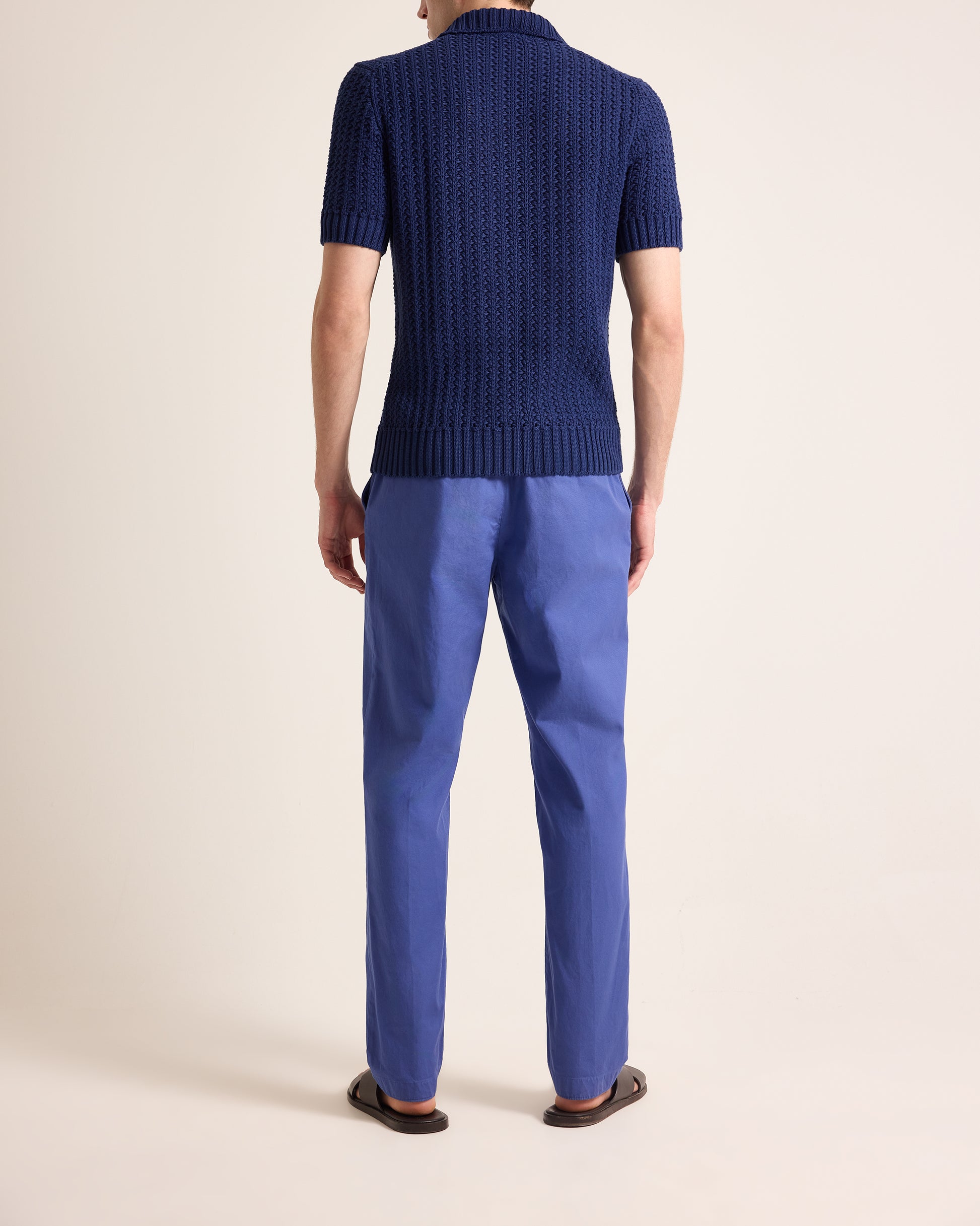 Person wearing a blue knitted sweater and pants on a beige background