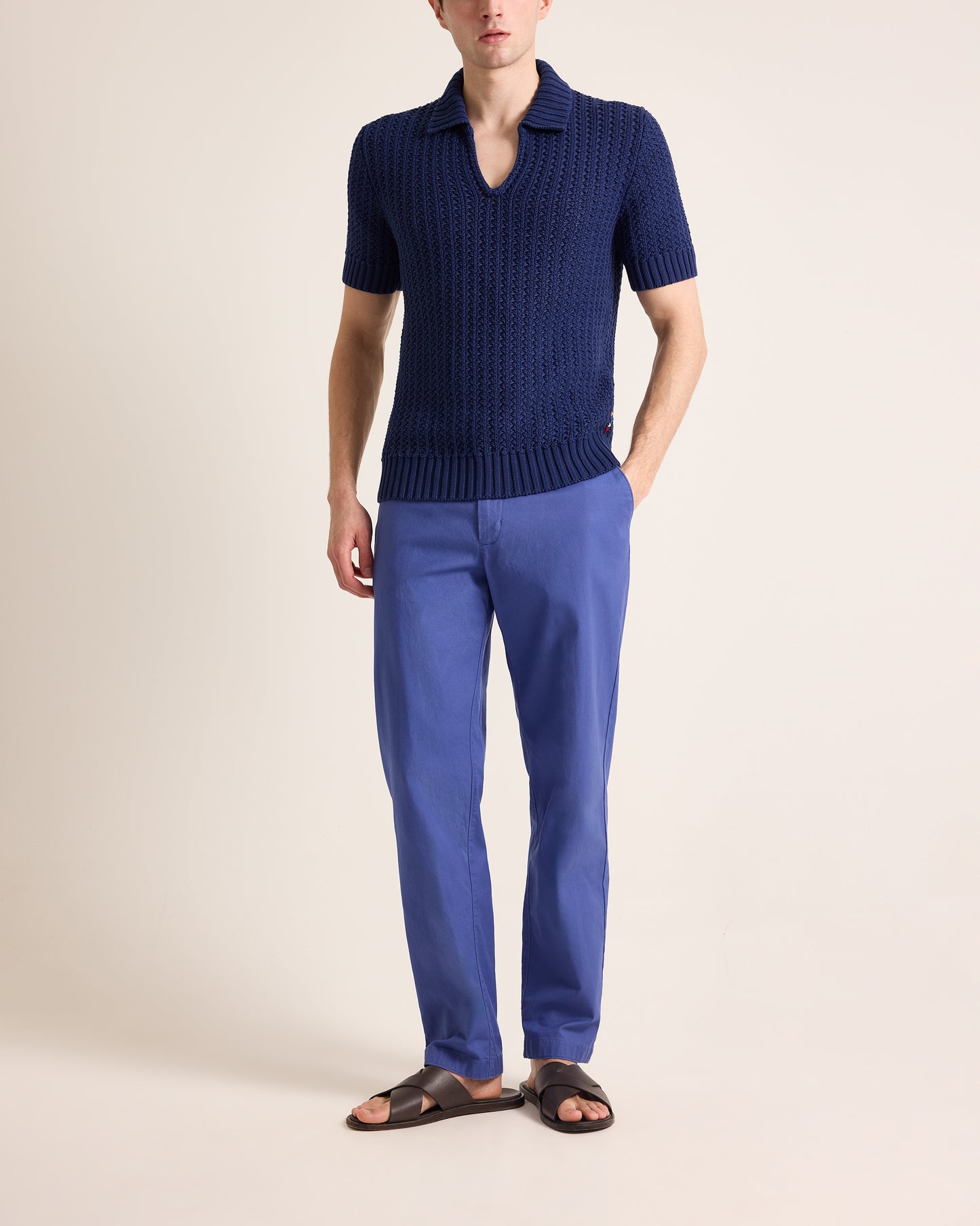 Person wearing a navy blue knitted polo shirt and matching pants on a beige background