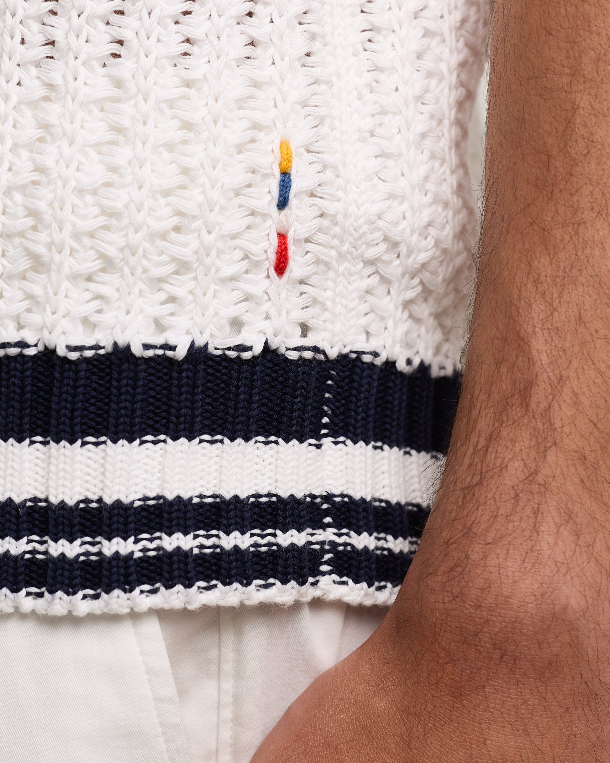 Close-up of a white polo top with blue and red stripes and a brand logo.