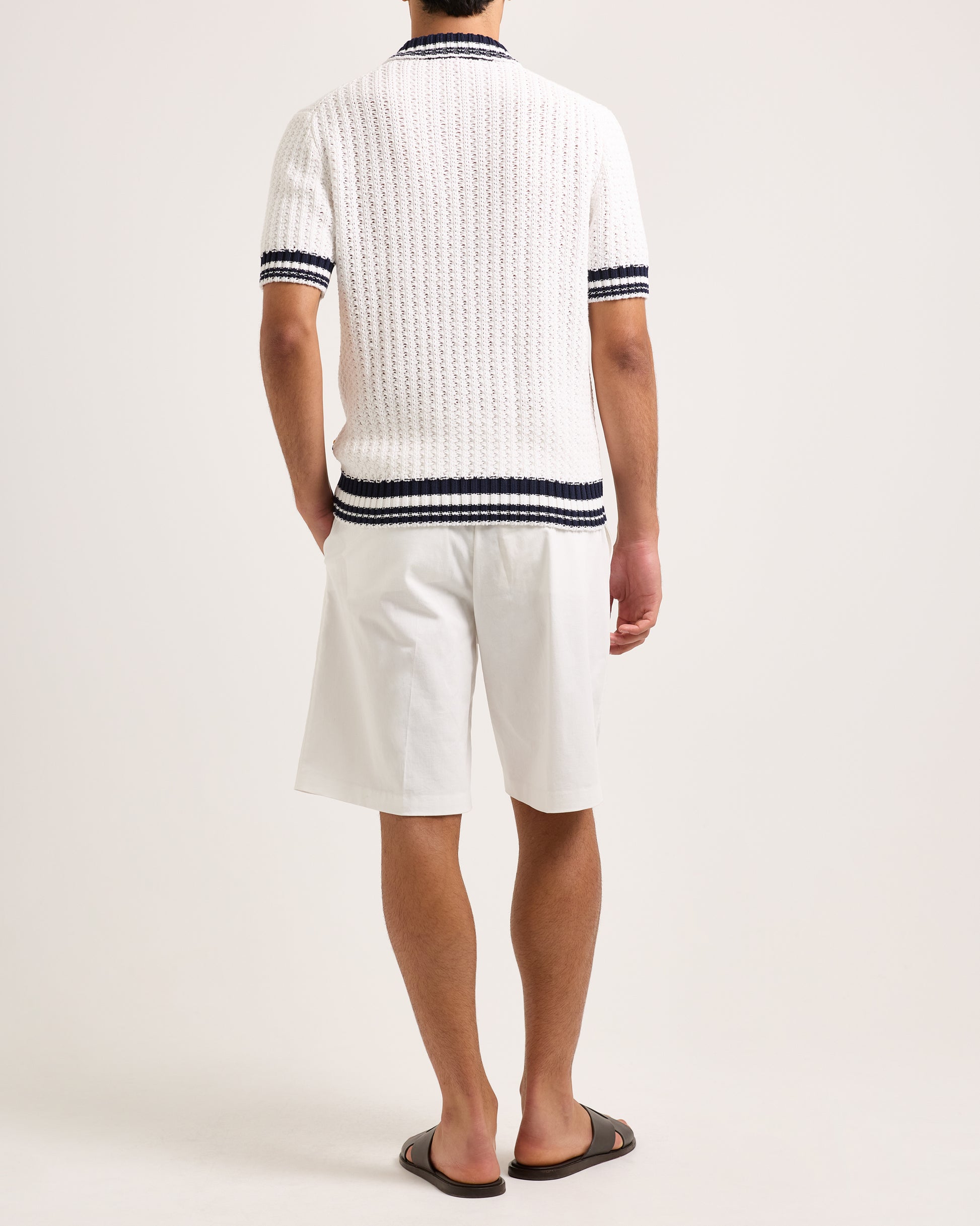 Model wearing white knitted polo shirt with black trim and white shorts on a white background