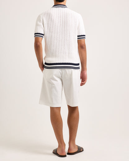 Model wearing white knitted polo shirt with black trim and white shorts on a white background