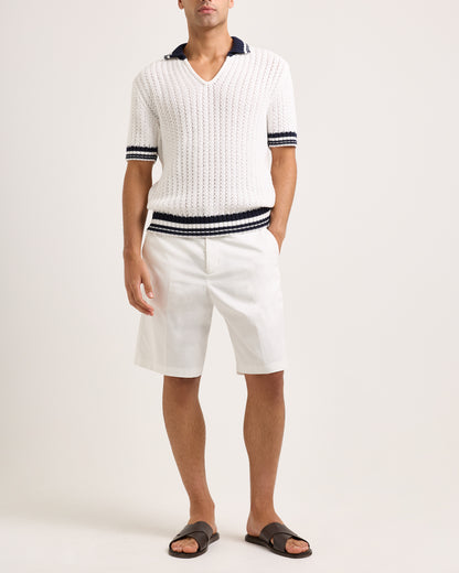 Model wearing white knitted polo shirt with black trim and white shorts on a white background