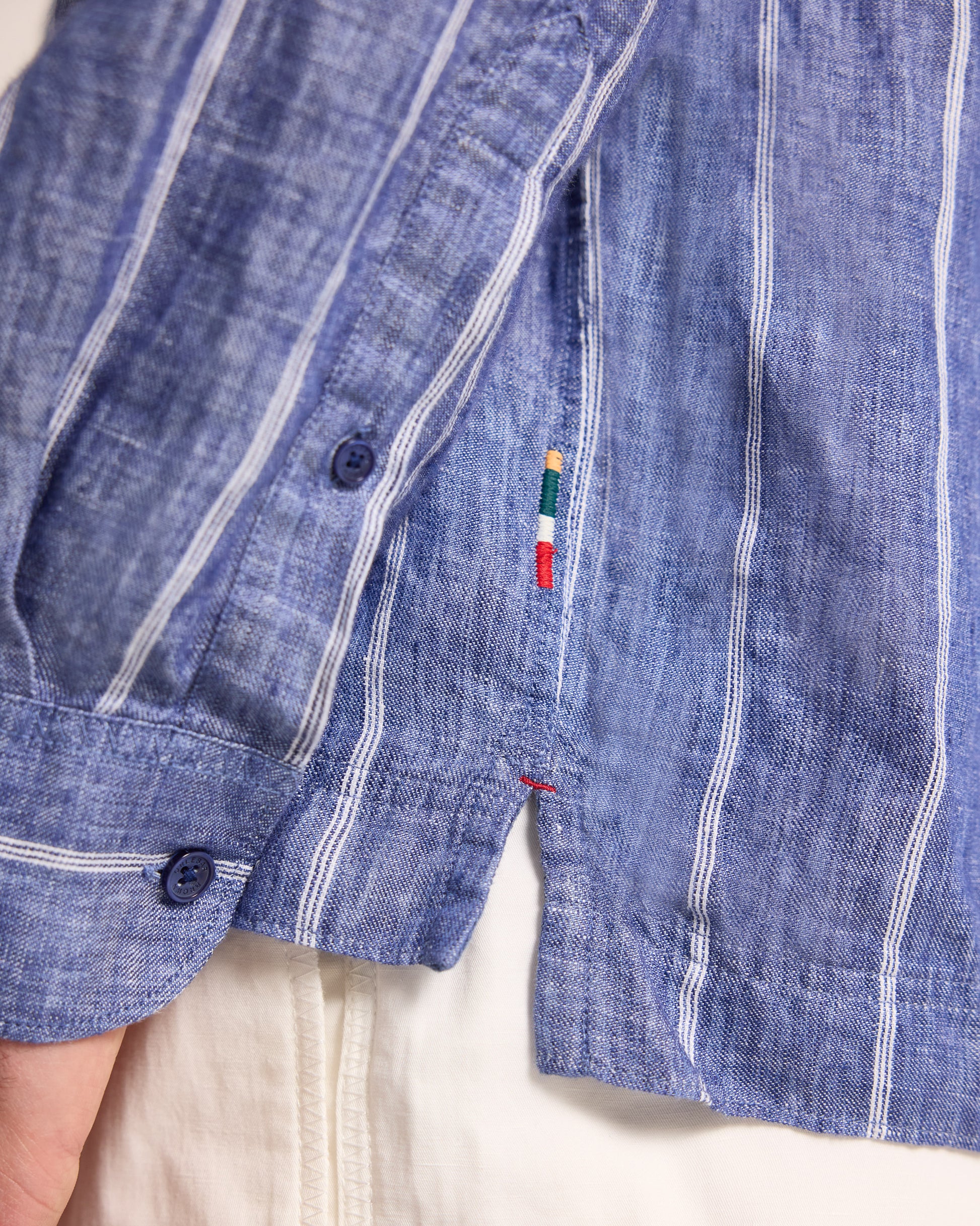 Close-up of a blue denim shirt with white stripes and a brand logo on a white background