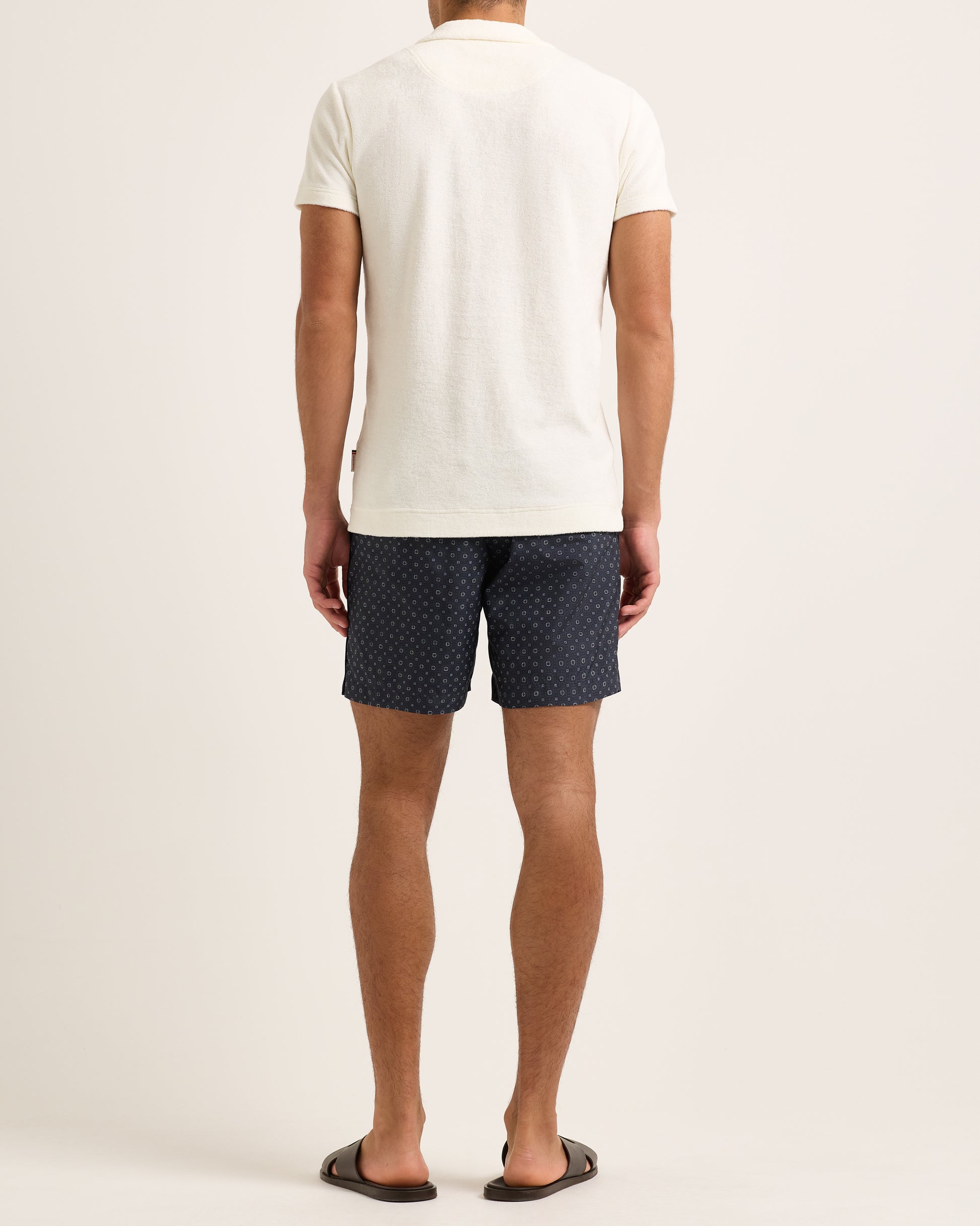 Person wearing a white towelling polo shirt and navy patterned shorts on a plain background