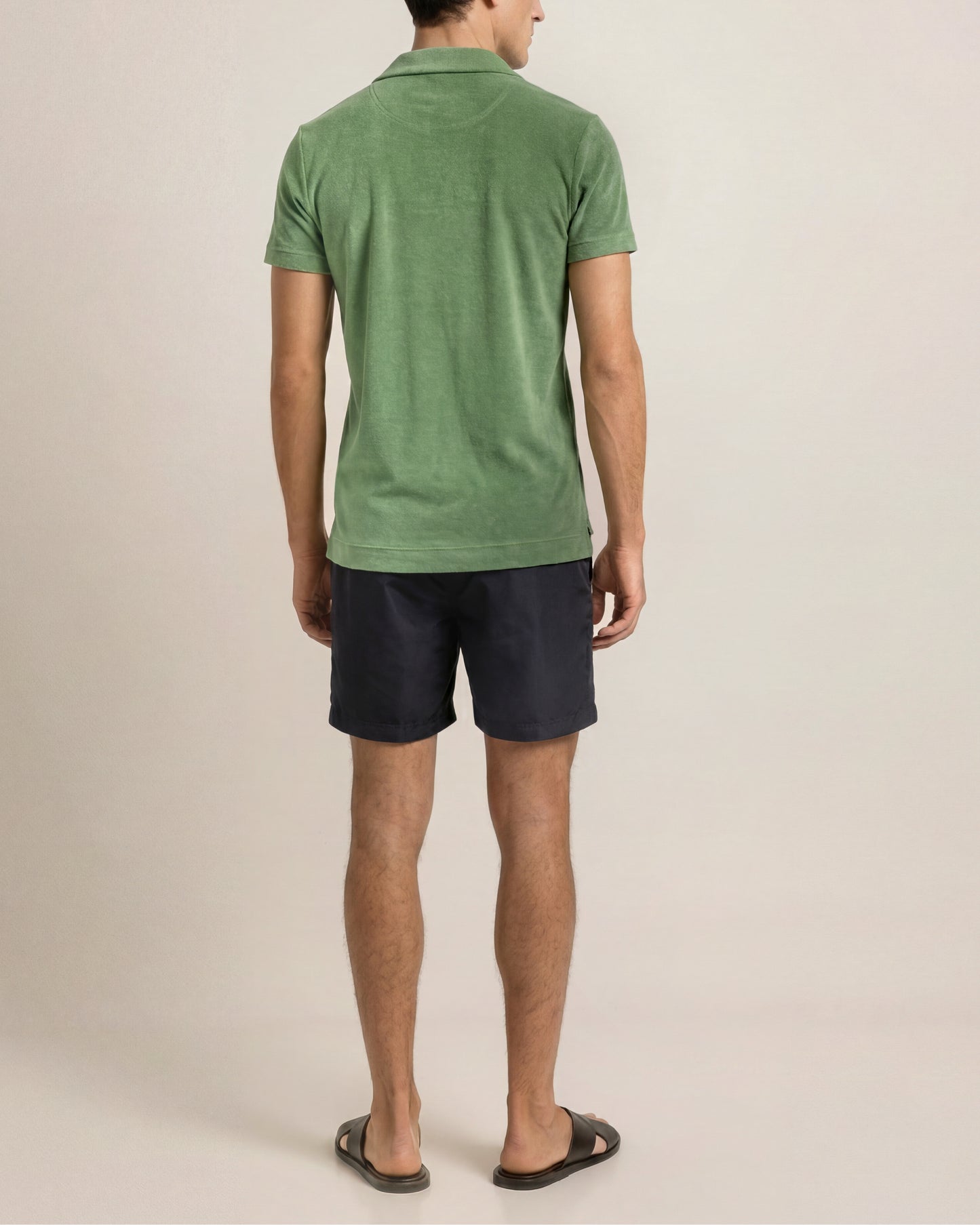 Man wearing a green polo shirt and black shorts on a beige background