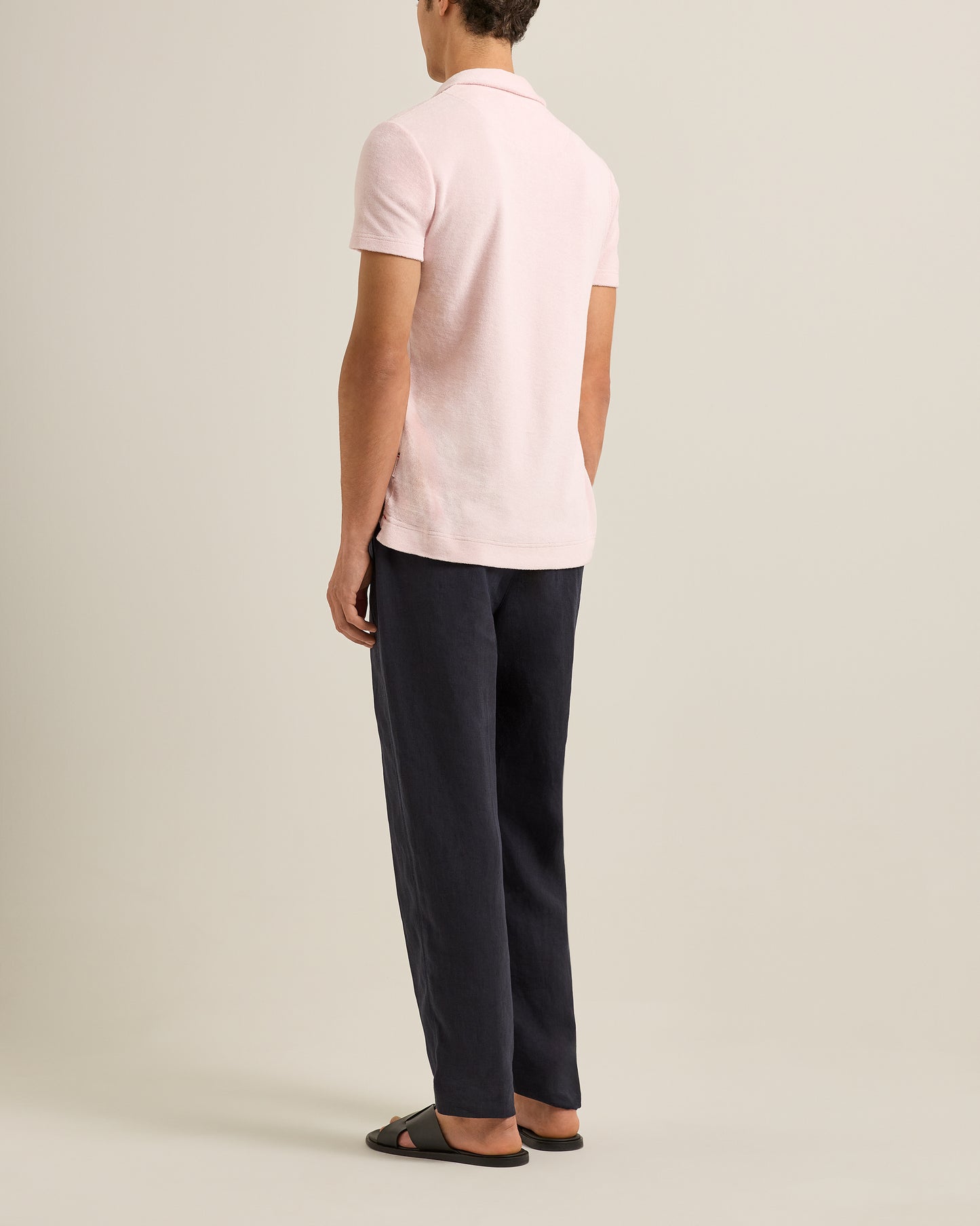 Person wearing a light pink polo shirt and dark pants on a plain background