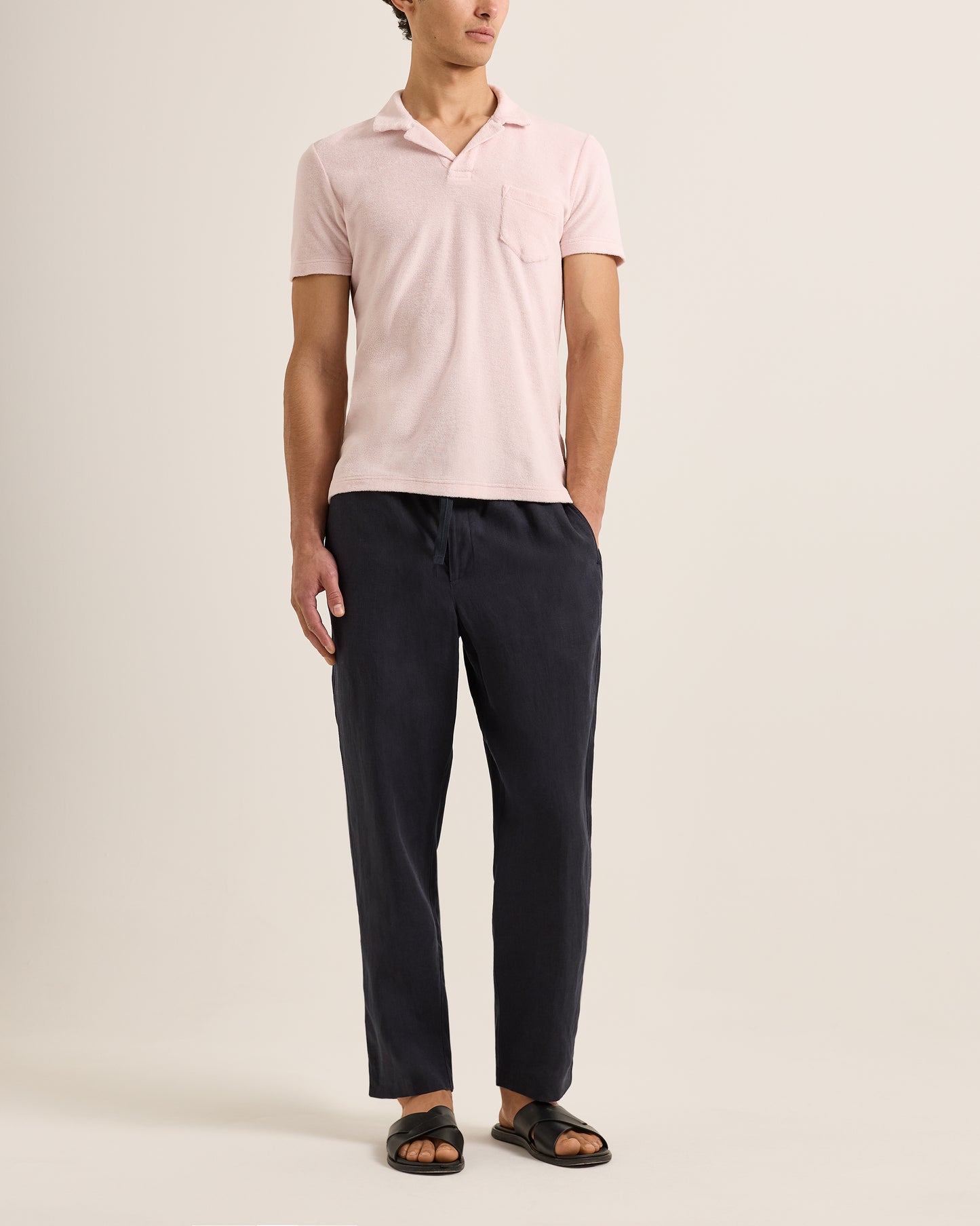 Person wearing a light pink polo shirt and dark pants on a plain background