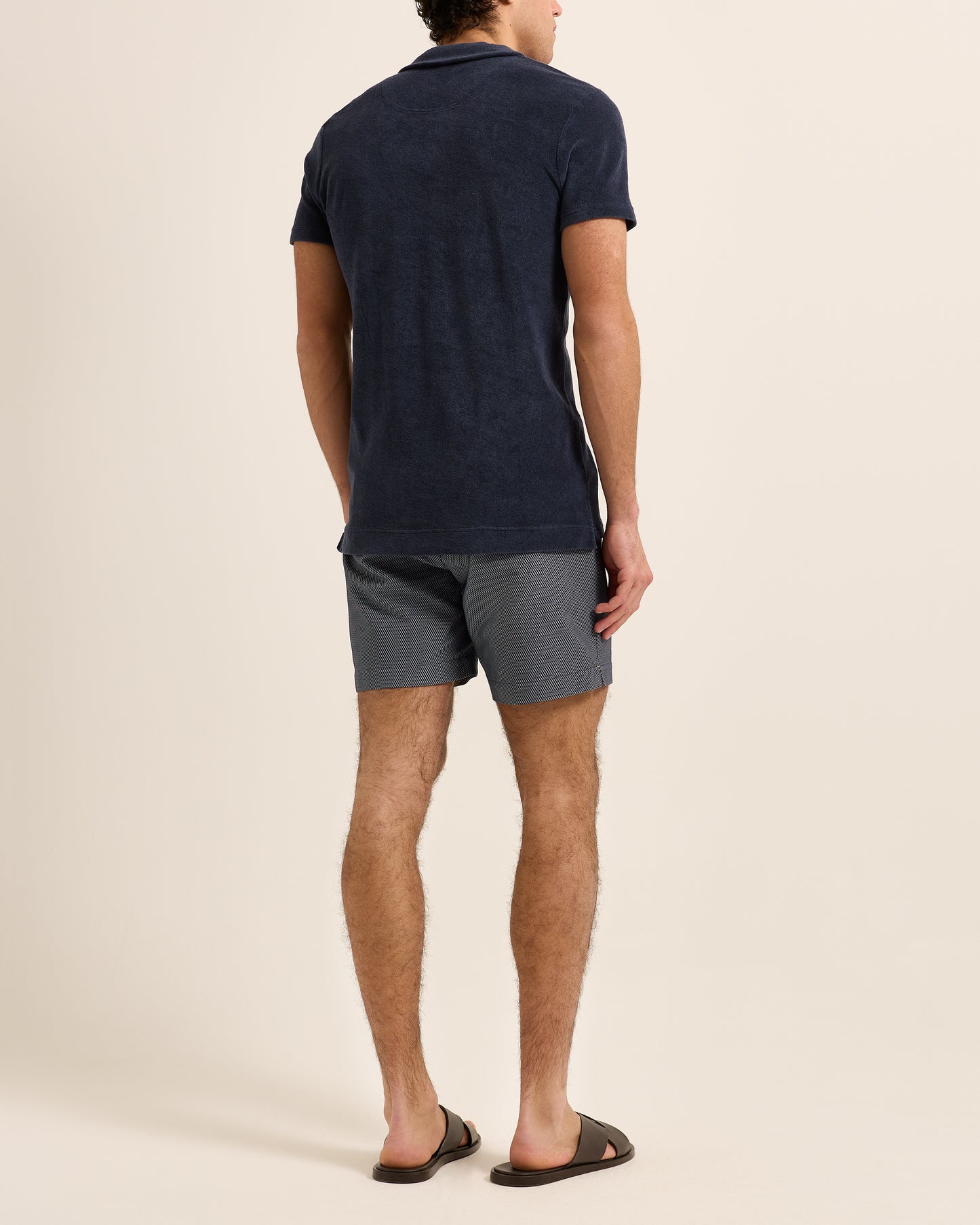 Man wearing navy polo shirt with navy patterned swim shorts on a plain background