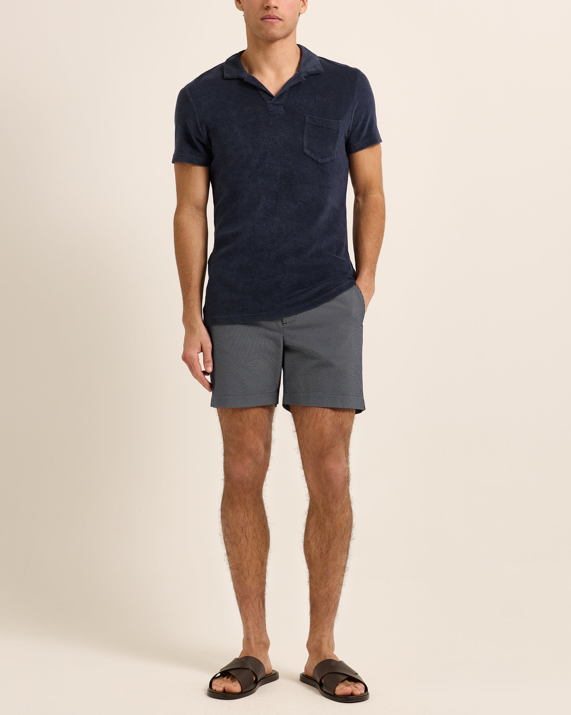 Man wearing navy polo shirt with navy patterned swim shorts on a plain background