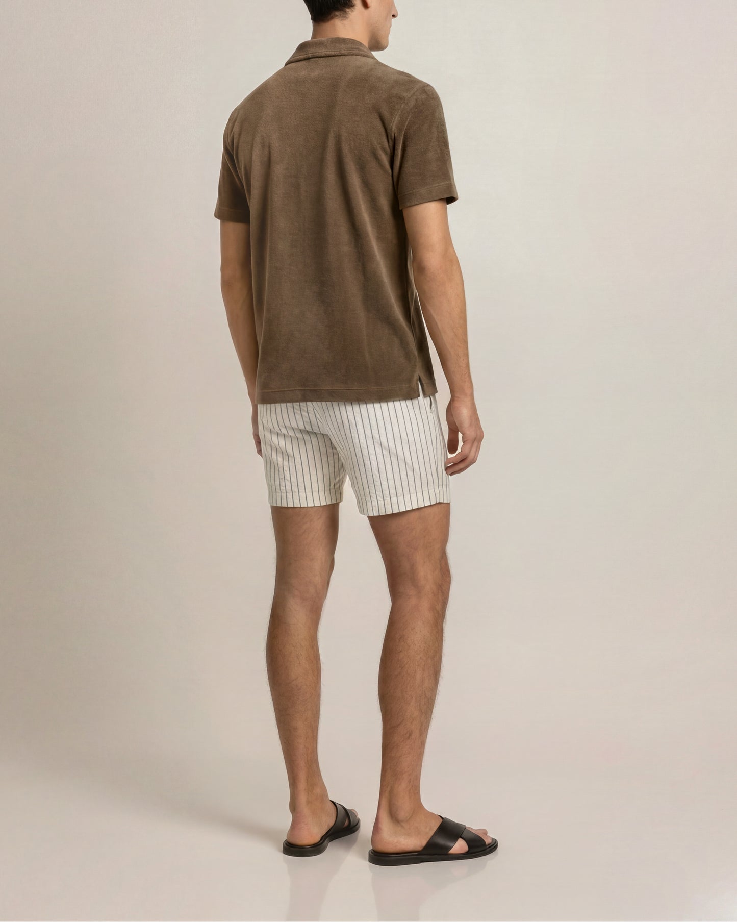 Man wearing a brown polo shirt and white striped shorts on a plain background