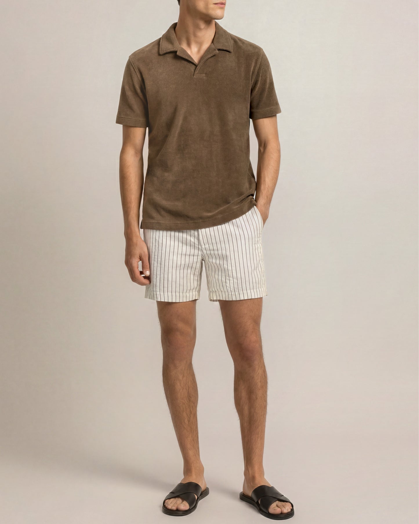 Man wearing a brown polo shirt and white striped shorts on a beige background