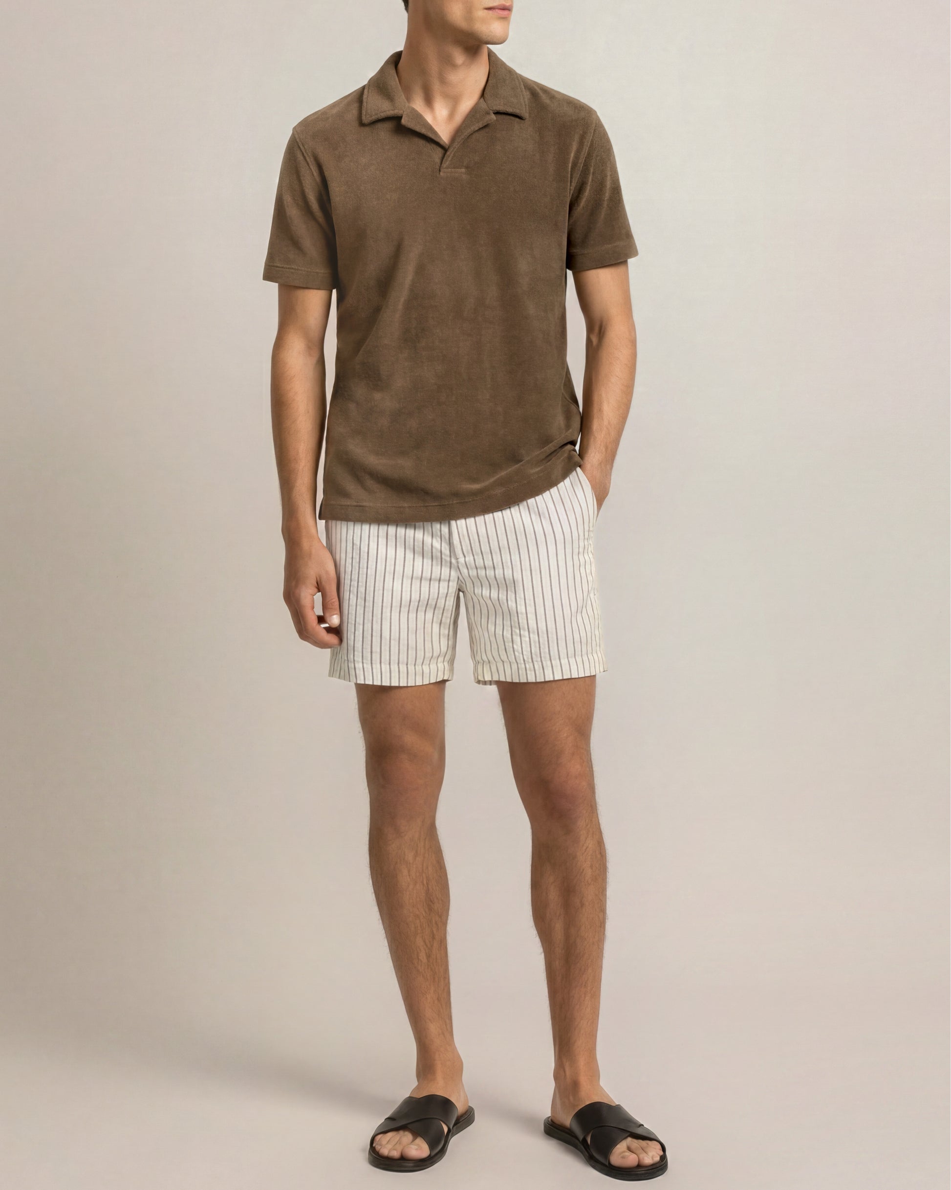 Man wearing a brown polo shirt and white striped shorts on a beige background