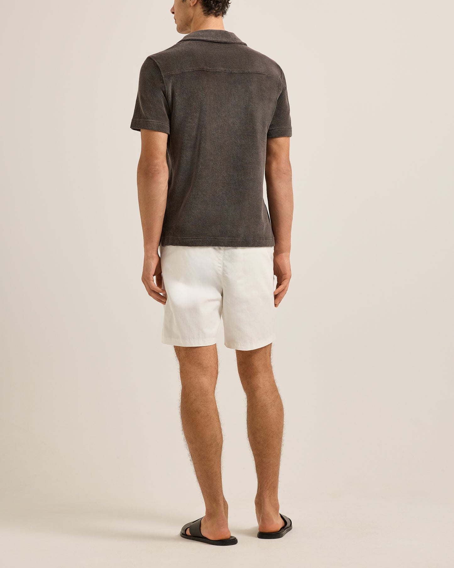 Man wearing a dark brown polo shirt and white shorts on a beige background