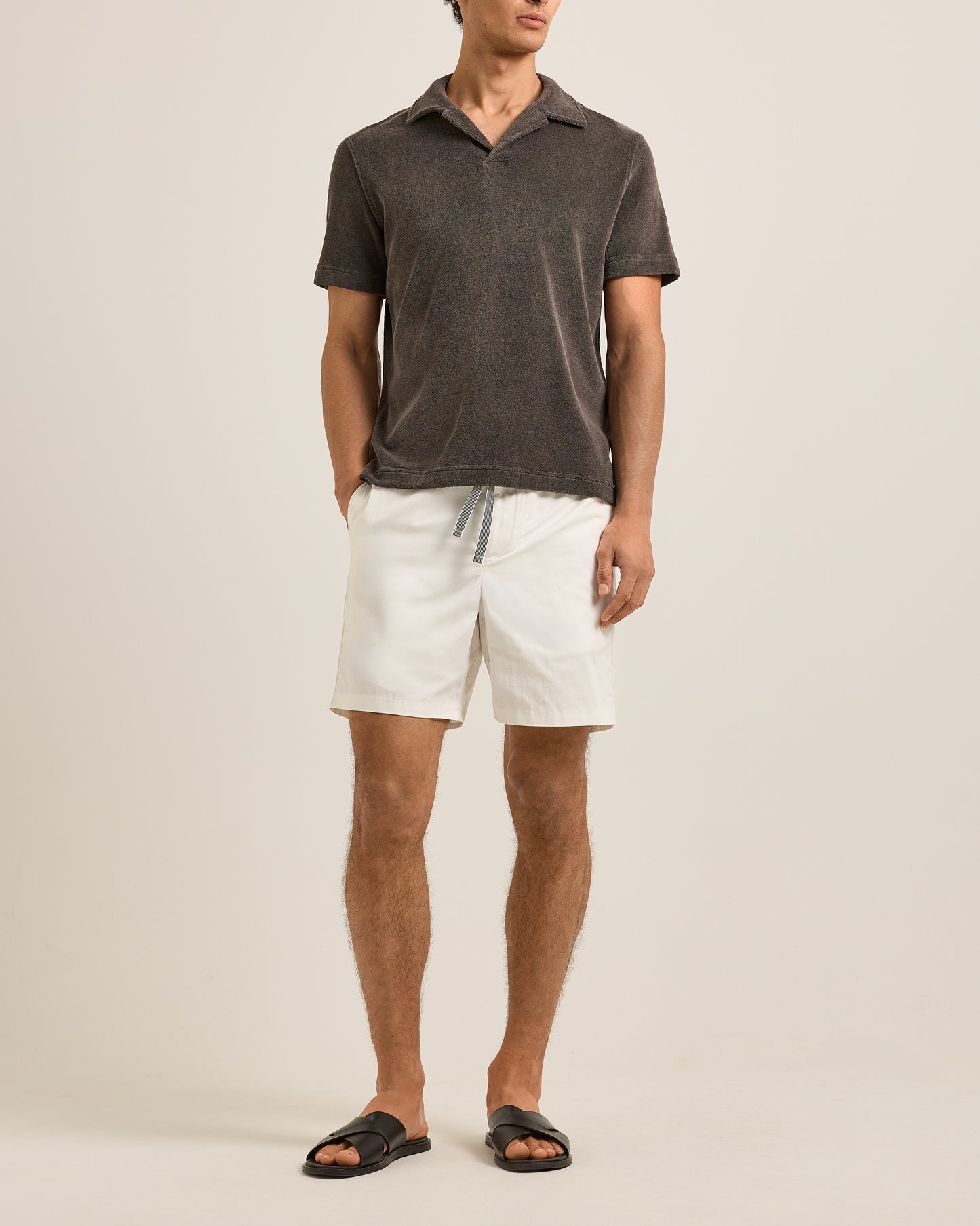 Man wearing a dark gray polo shirt and white shorts on a beige background