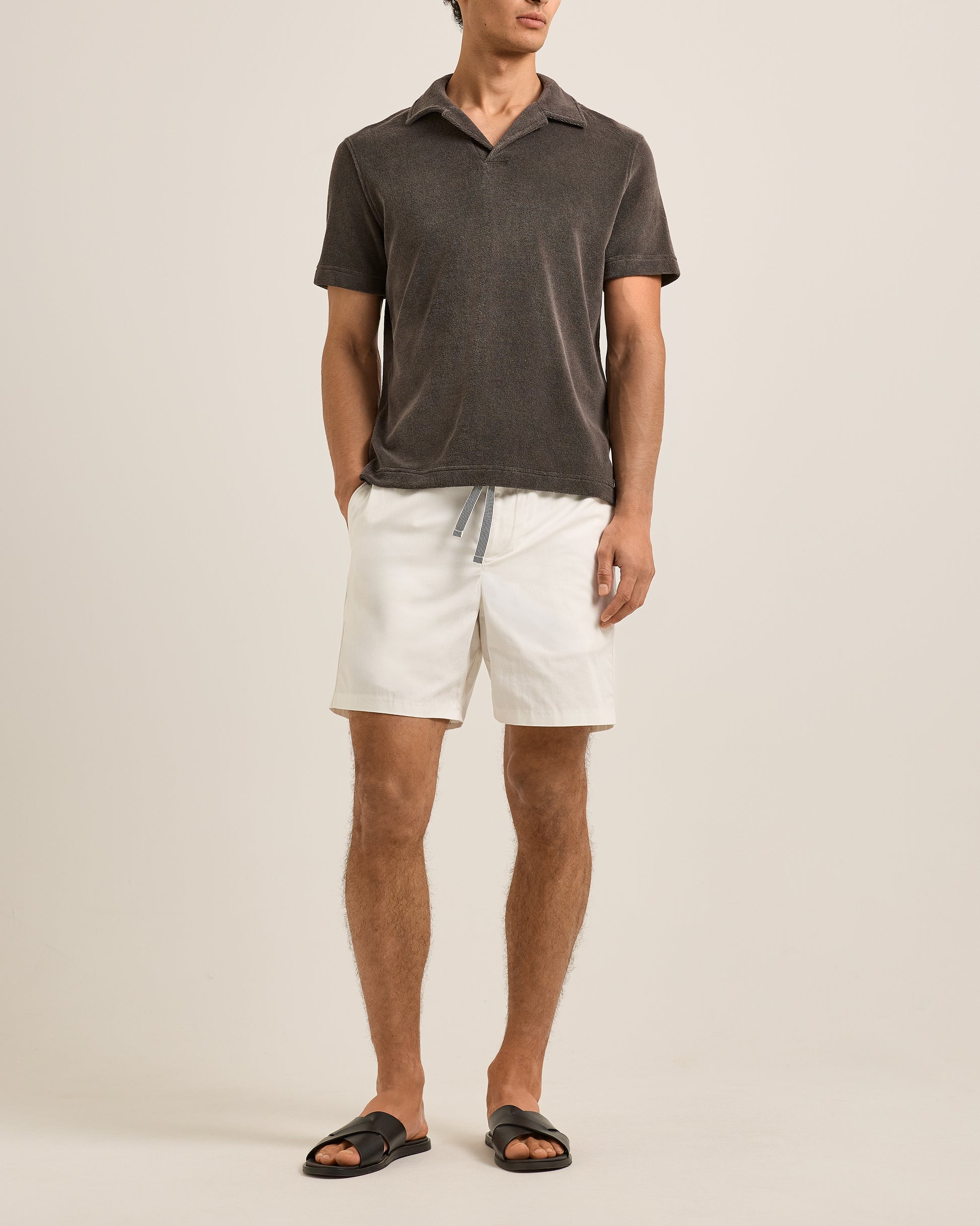 Man wearing a dark gray polo shirt and white shorts on a beige background