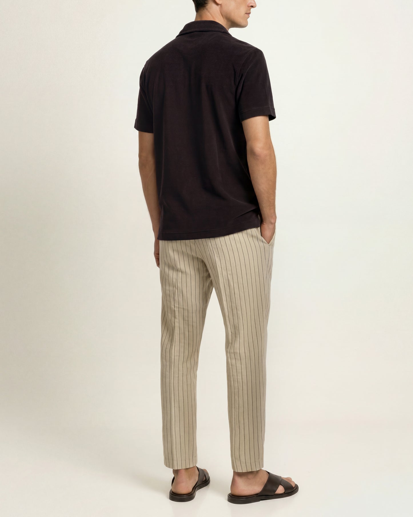 Man wearing dark brown polo shirt with striped beige trousers on a plain background