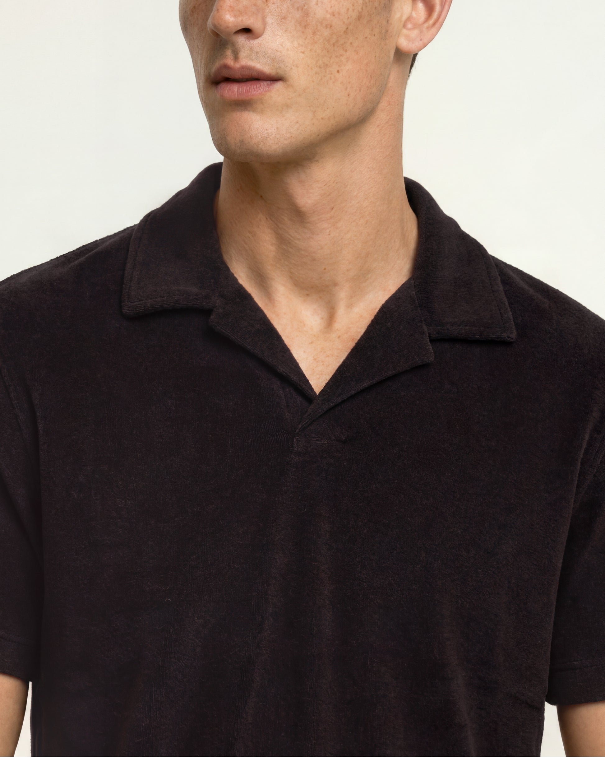Close-up of a man wearing a dark brown short-sleeve polo shirt with a textured knit fabric, set against a plain light background.