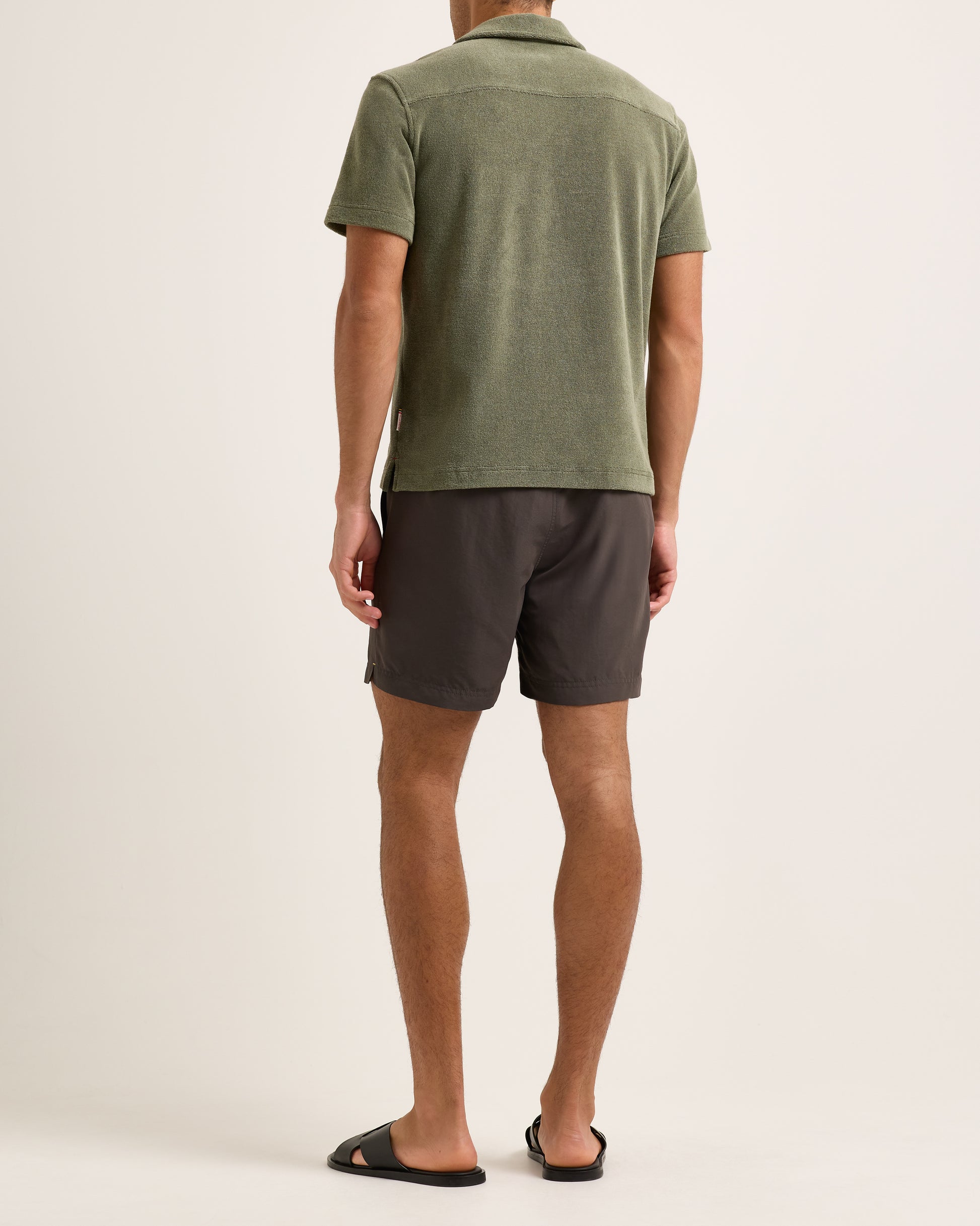 Model wearing dark green towelling polo shirt with brown shorts on a white background