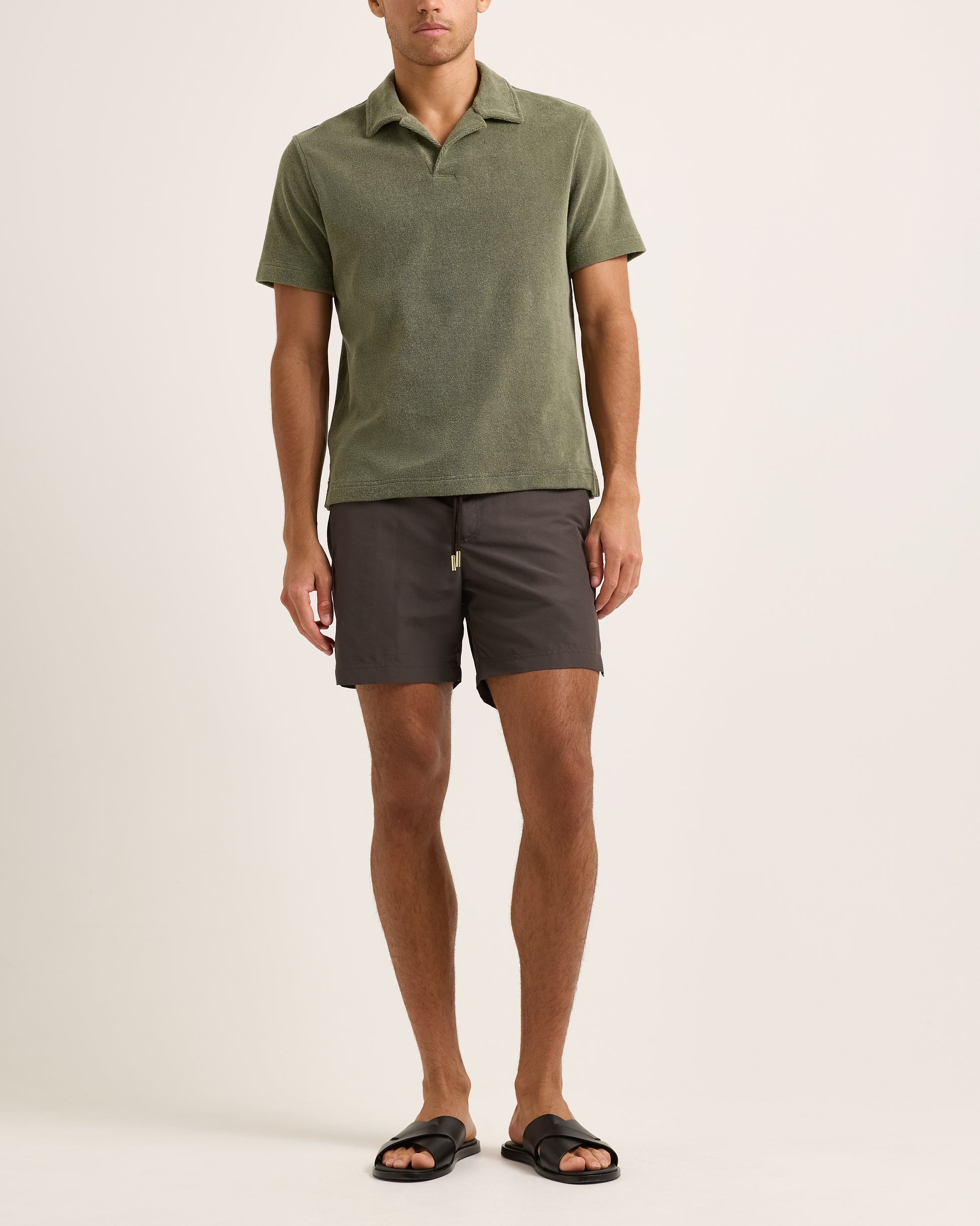 Model wearing dark green towelling polo shirt with brown shorts on a white background