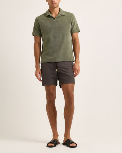 Model wearing dark green towelling polo shirt with brown shorts on a white background