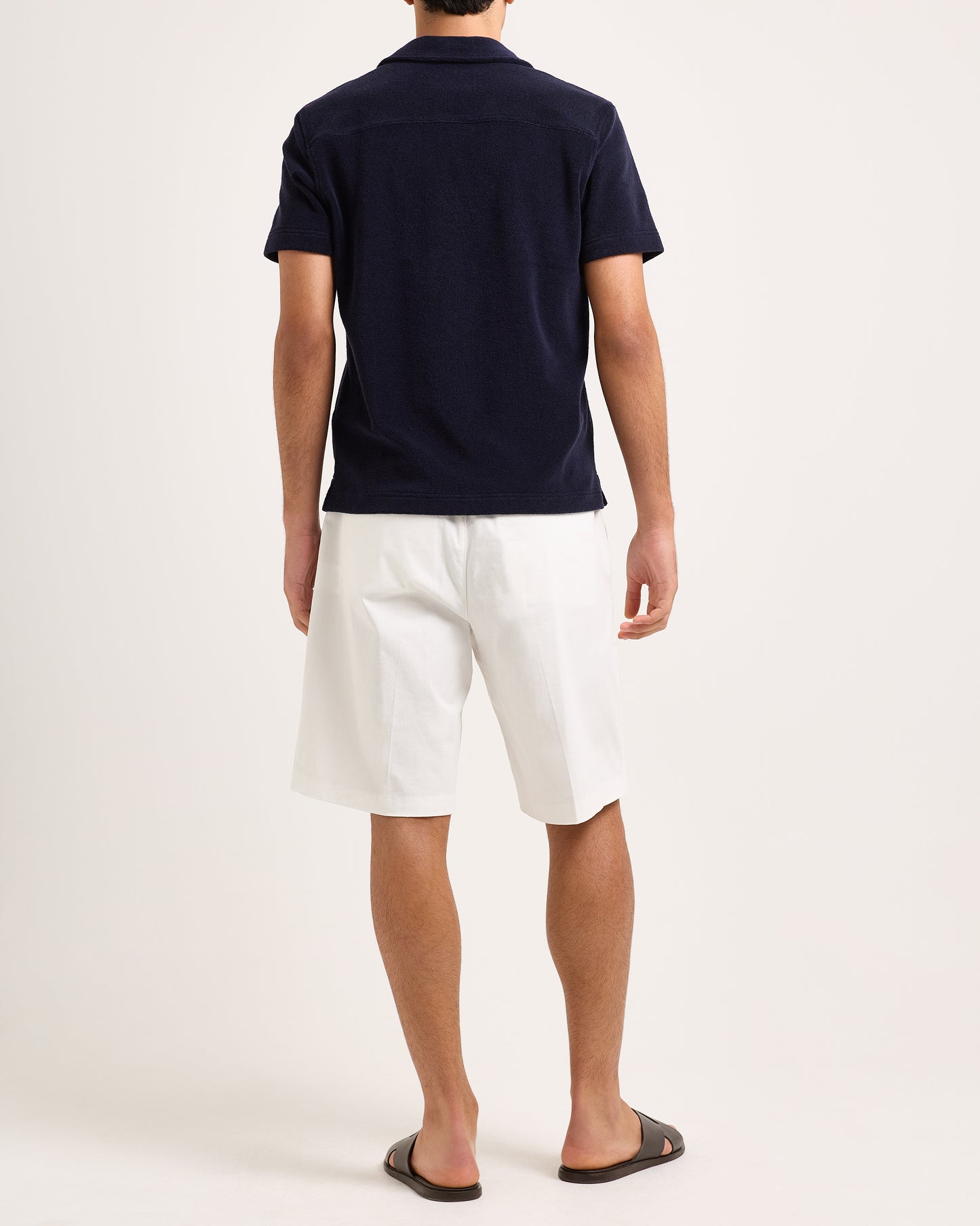 Model wearing navy towelling polo shirt with white shorts on a white background