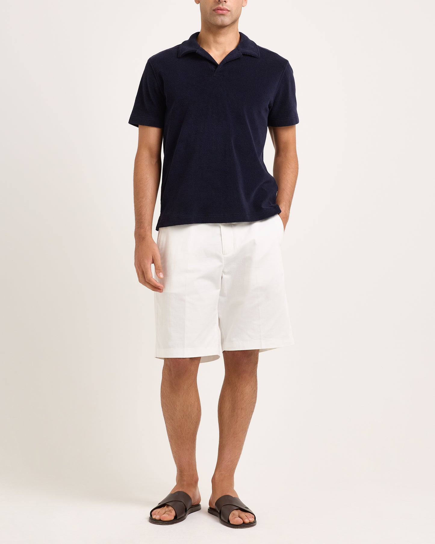 Model wearing navy towelling polo shirt with white shorts on a white background