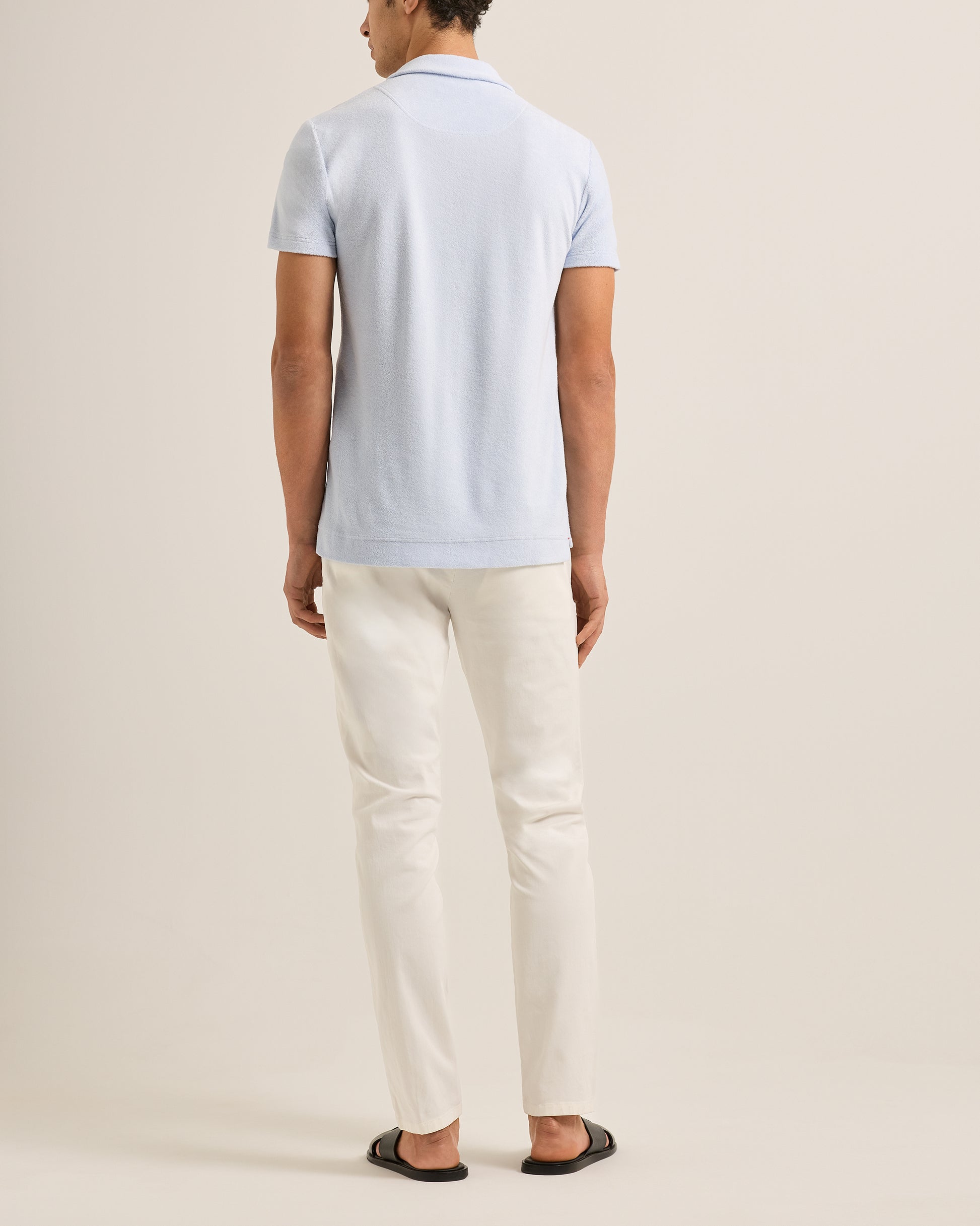 Person wearing a light blue polo shirt and white pants on a beige background