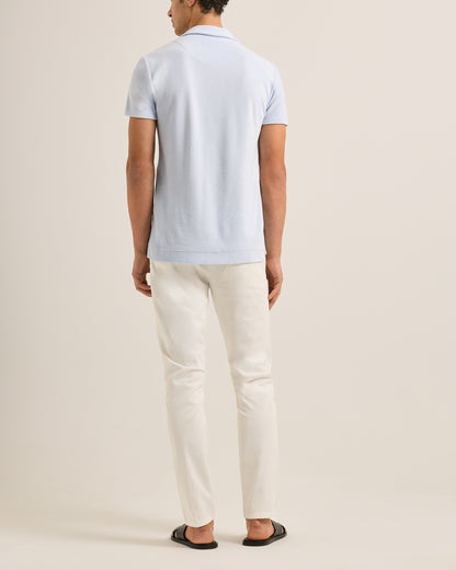 Person wearing a light blue polo shirt and white pants on a beige background
