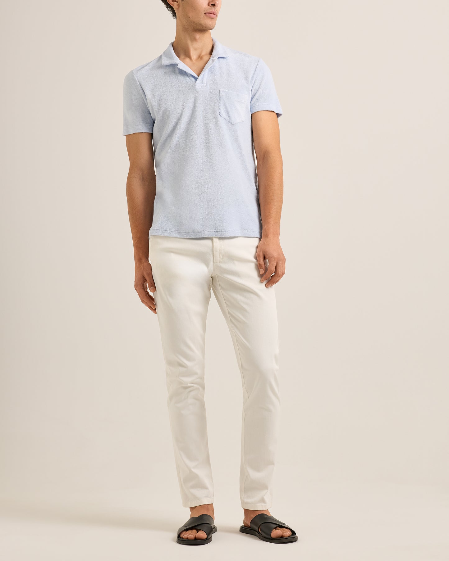 Man wearing a light blue polo shirt and white pants on a beige background