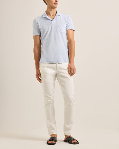 Man wearing a light blue polo shirt and white pants on a beige background