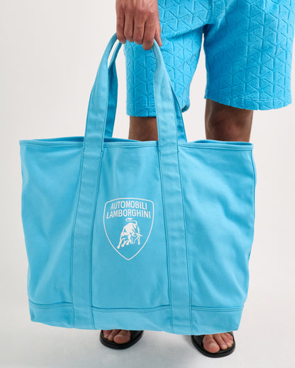 Person holding a blue tote bag with Automobili Lamborghini logo on a light gray background