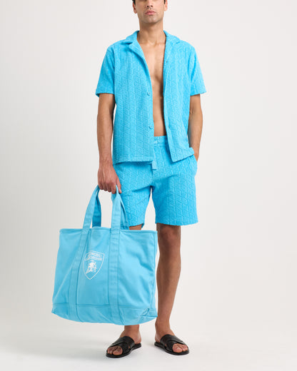 Man wearing a blue textured shirt and shorts holding a matching blue tote bag on a white background