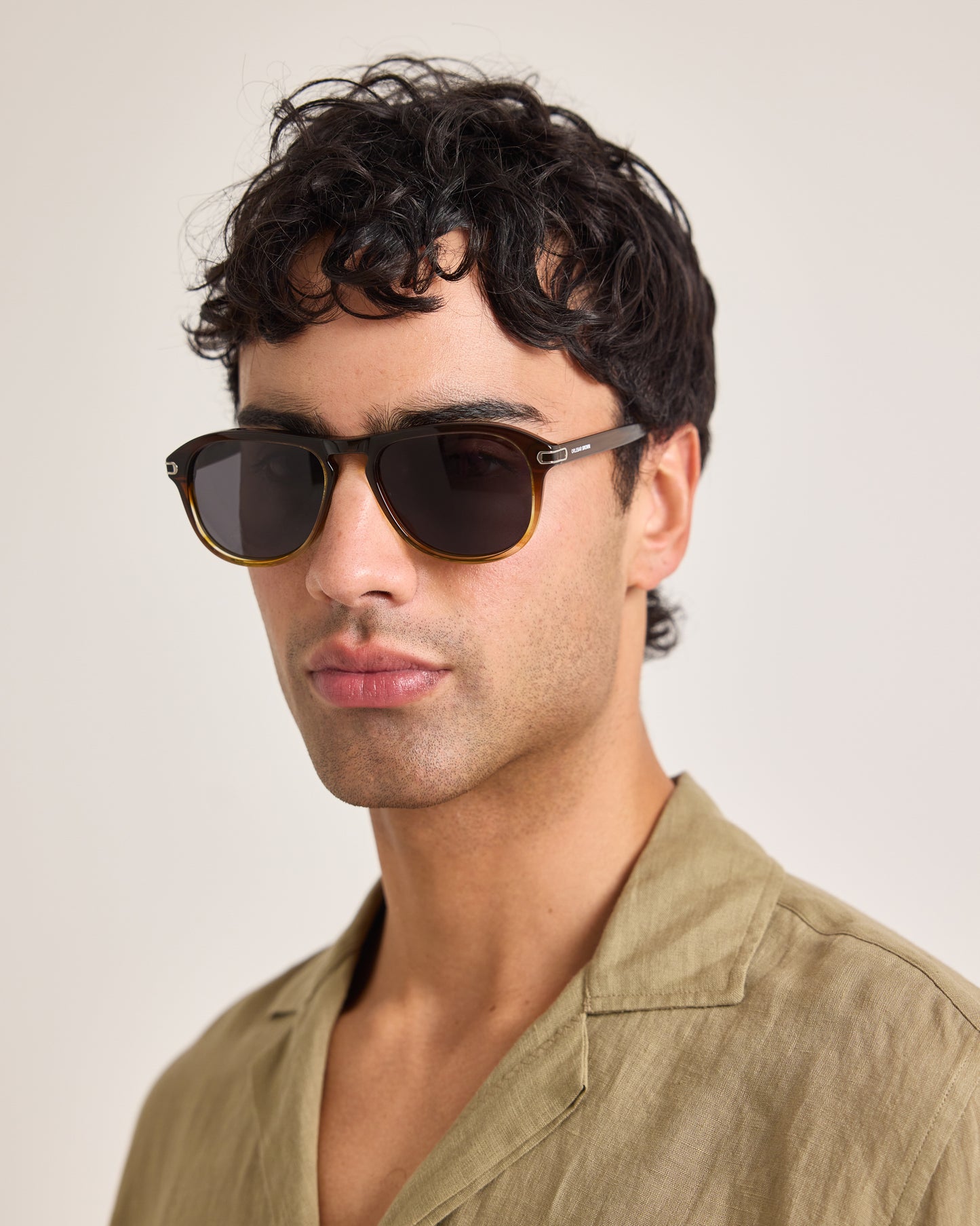 Man wearing dark sunglasses and a beige shirt against a plain background