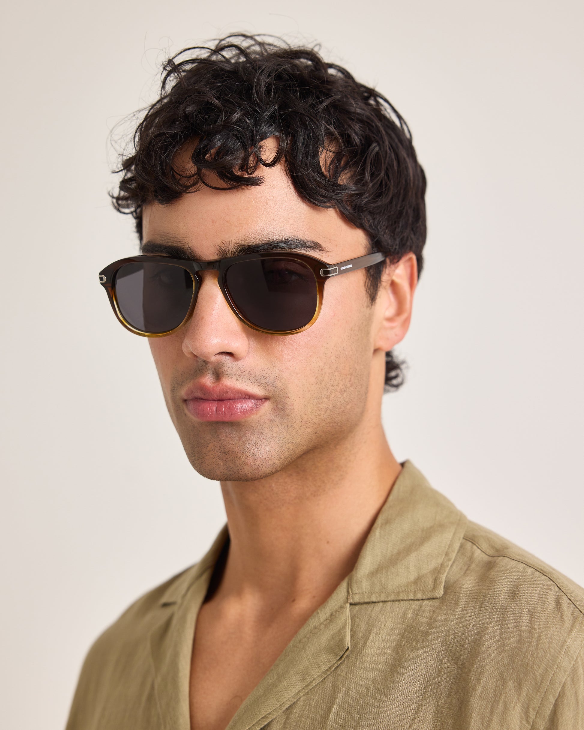 Man wearing dark sunglasses and a beige shirt against a plain background