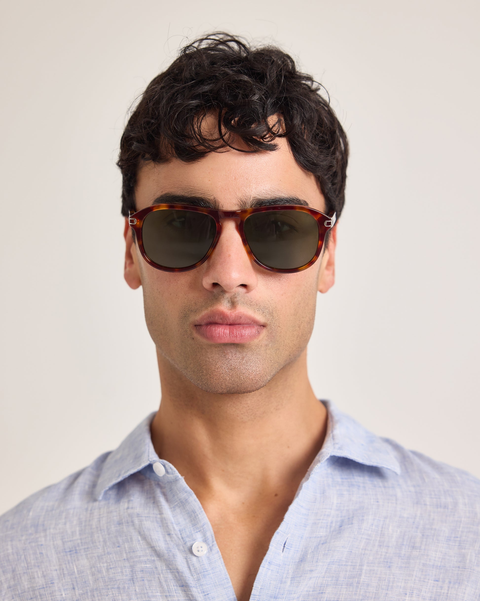 Man wearing sunglasses and a light blue shirt against a plain background