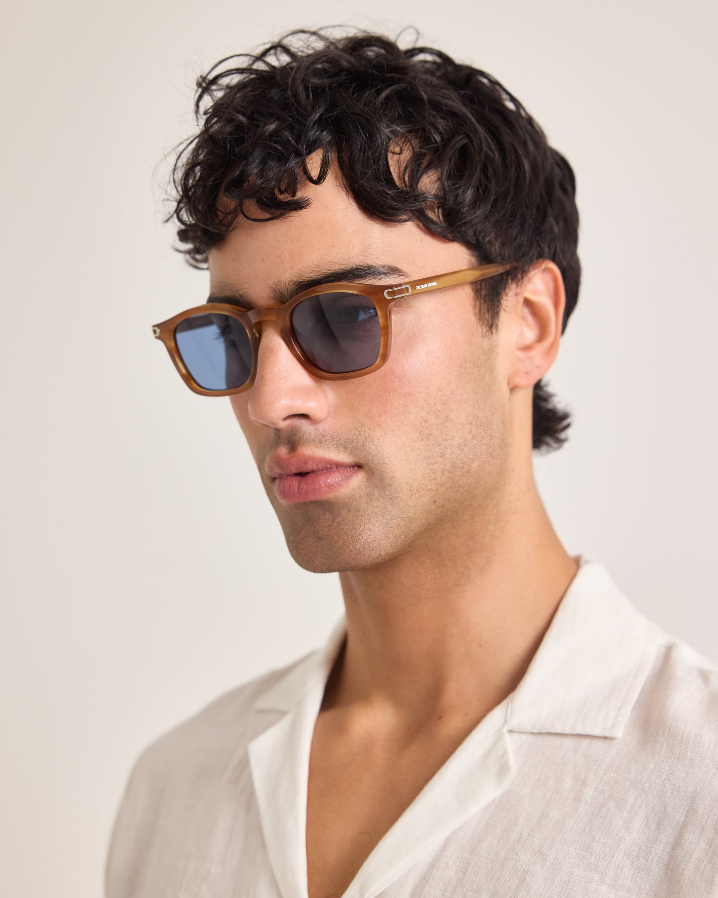 Man wearing sunglasses and a white shirt against a plain background
