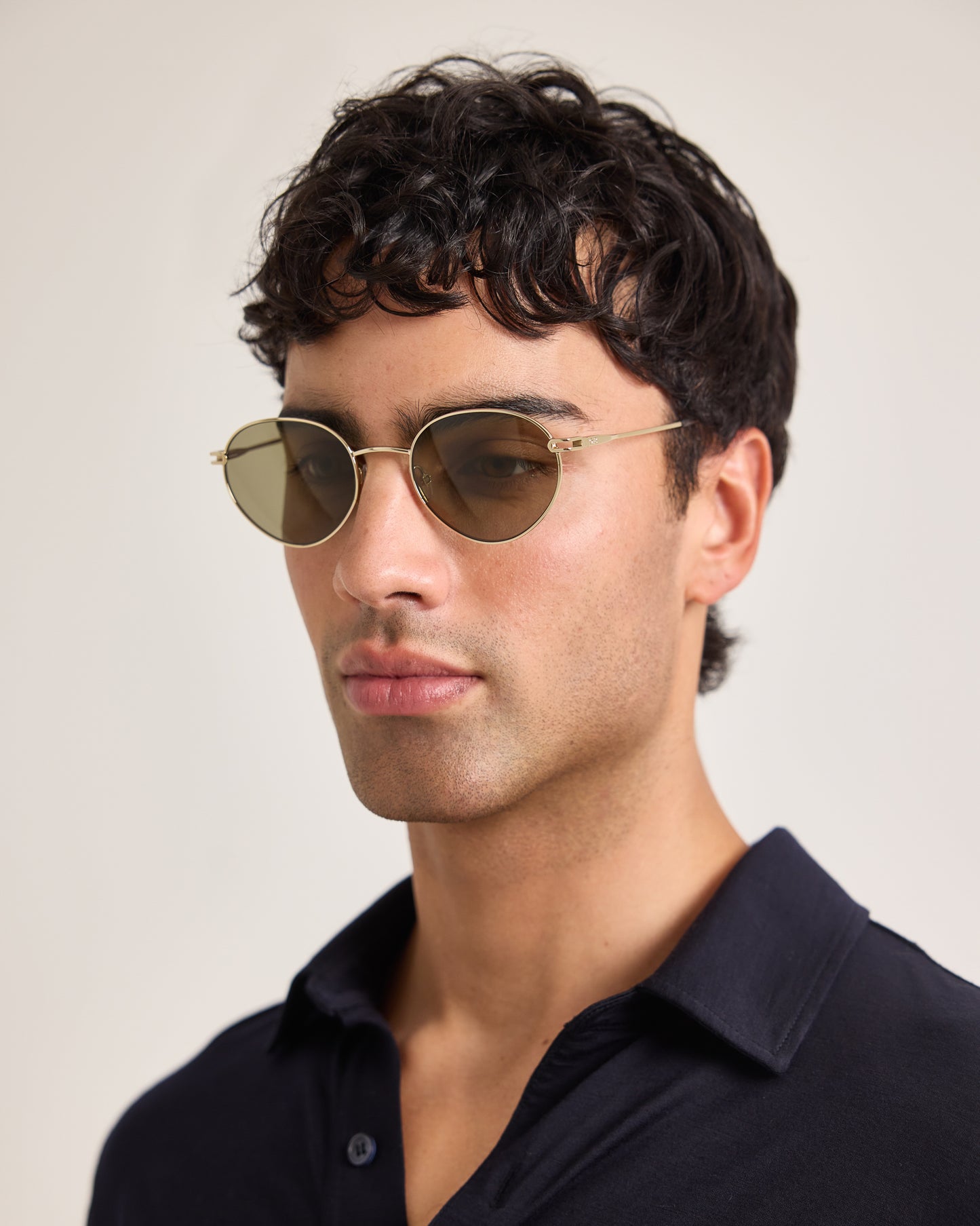 Man wearing gold-rimmed sunglasses with a neutral background