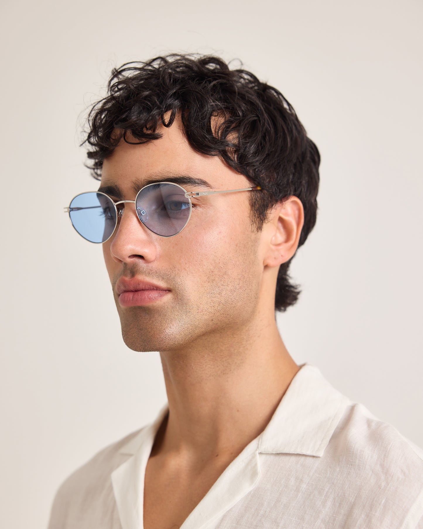 Man wearing round sunglasses and a white shirt against a plain background