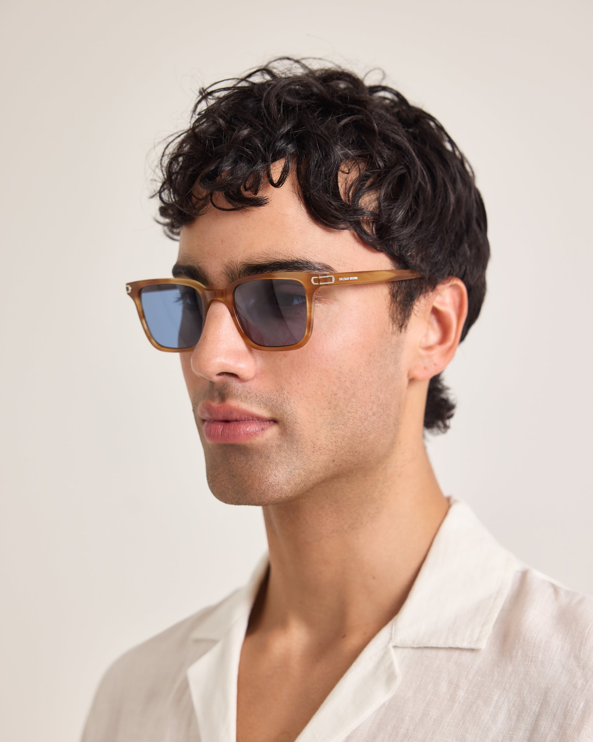 Man wearing brown sunglasses and a white shirt against a plain background