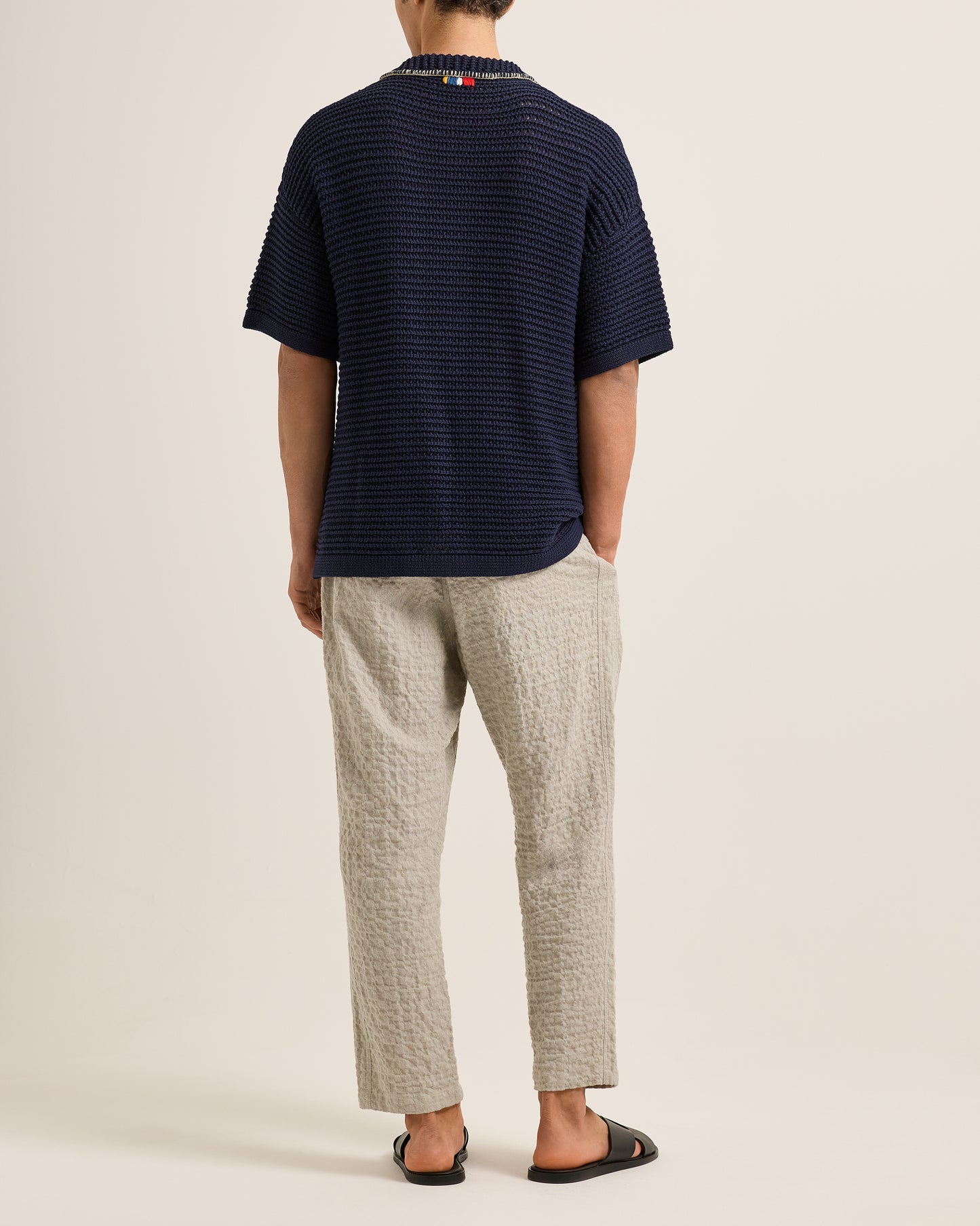 Person wearing a navy striped shirt and light-colored pants on a plain background